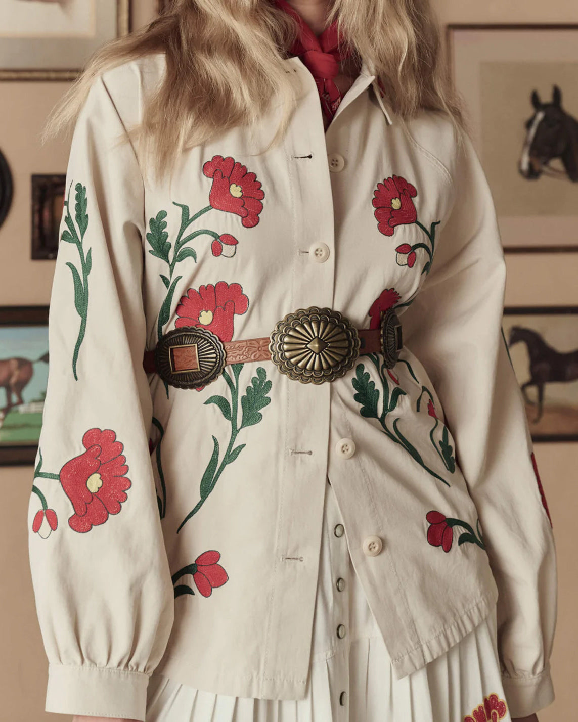 Person wearing a cream-colored shirt with red floral embroidery, accessorized with a belt.