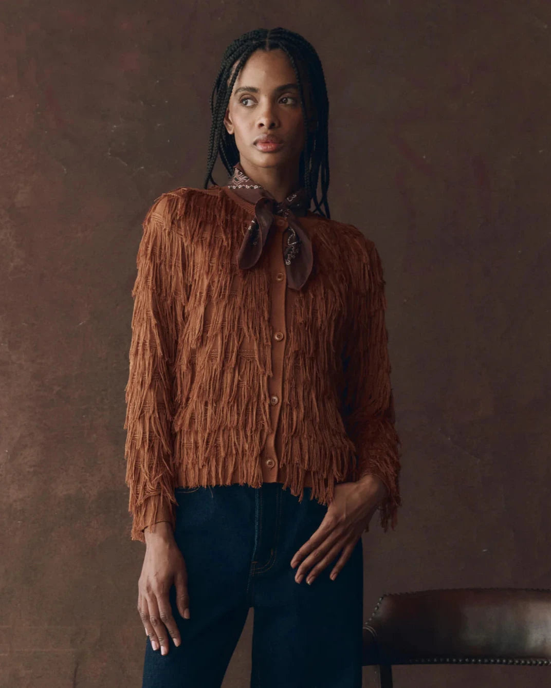 Person wearing a brown fringed shirt against a brown background