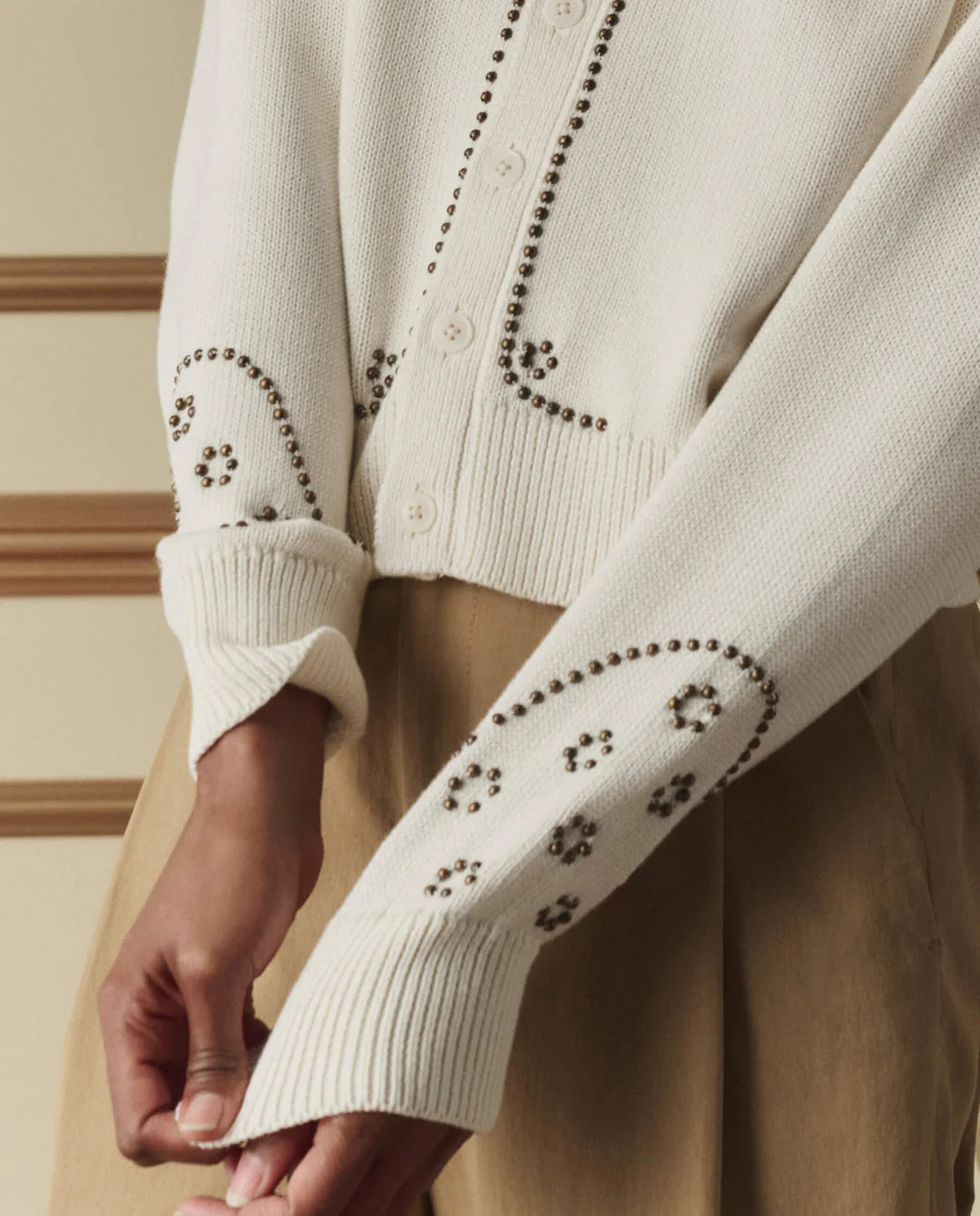 Close-up of a cream-colored sweater with decorative cut-out patterns on the sleeves.
