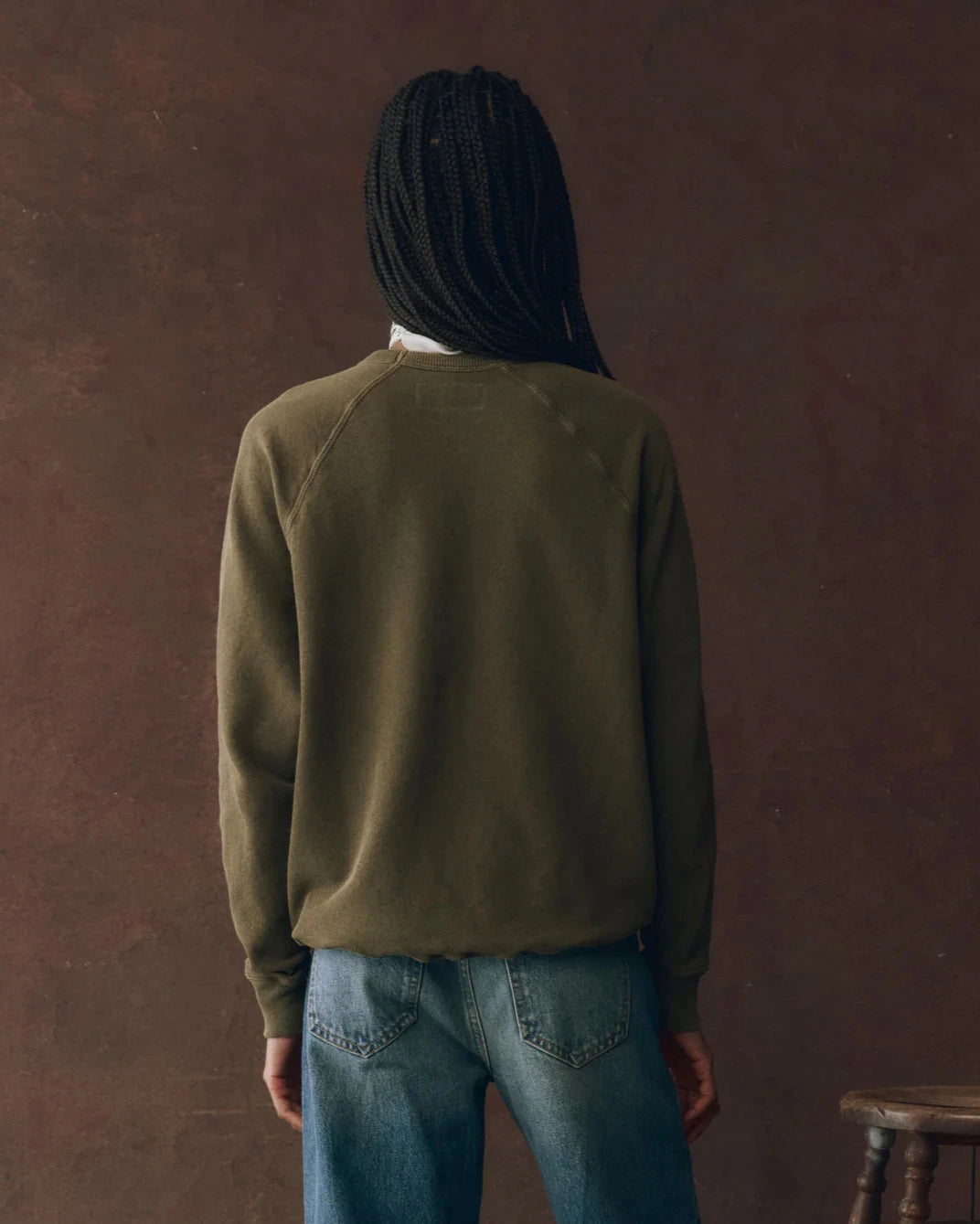 Person wearing a green sweatshirt and blue jeans against a brown background