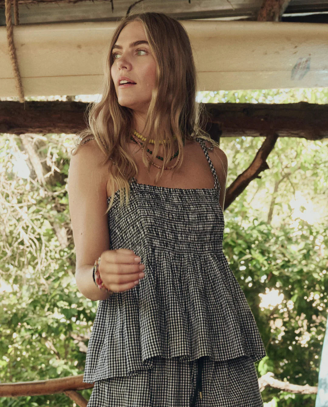 Woman wearing a checkered top and pants standing outdoors with greenery in the background