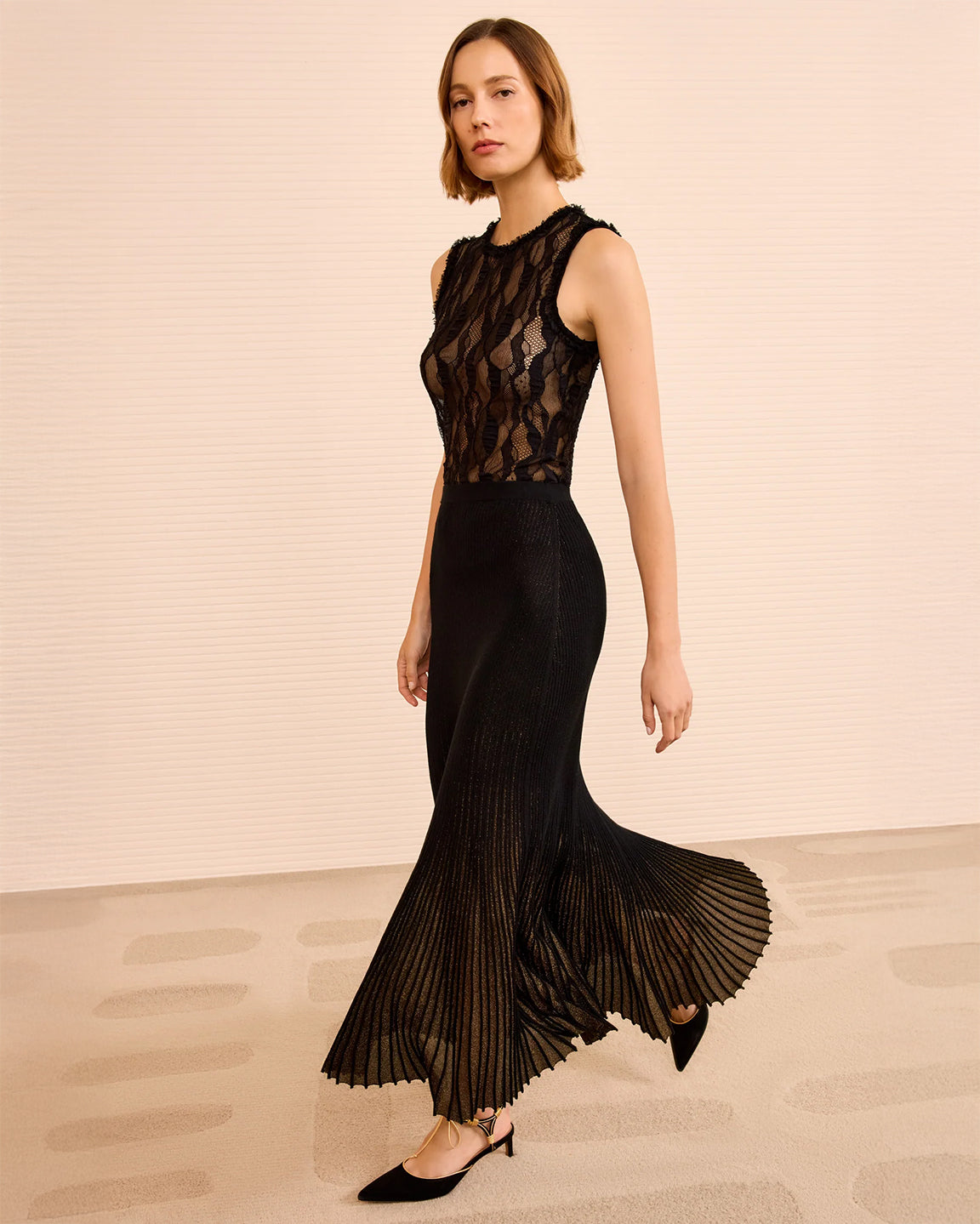 Woman wearing a black lace top and pleated skirt on a beige background