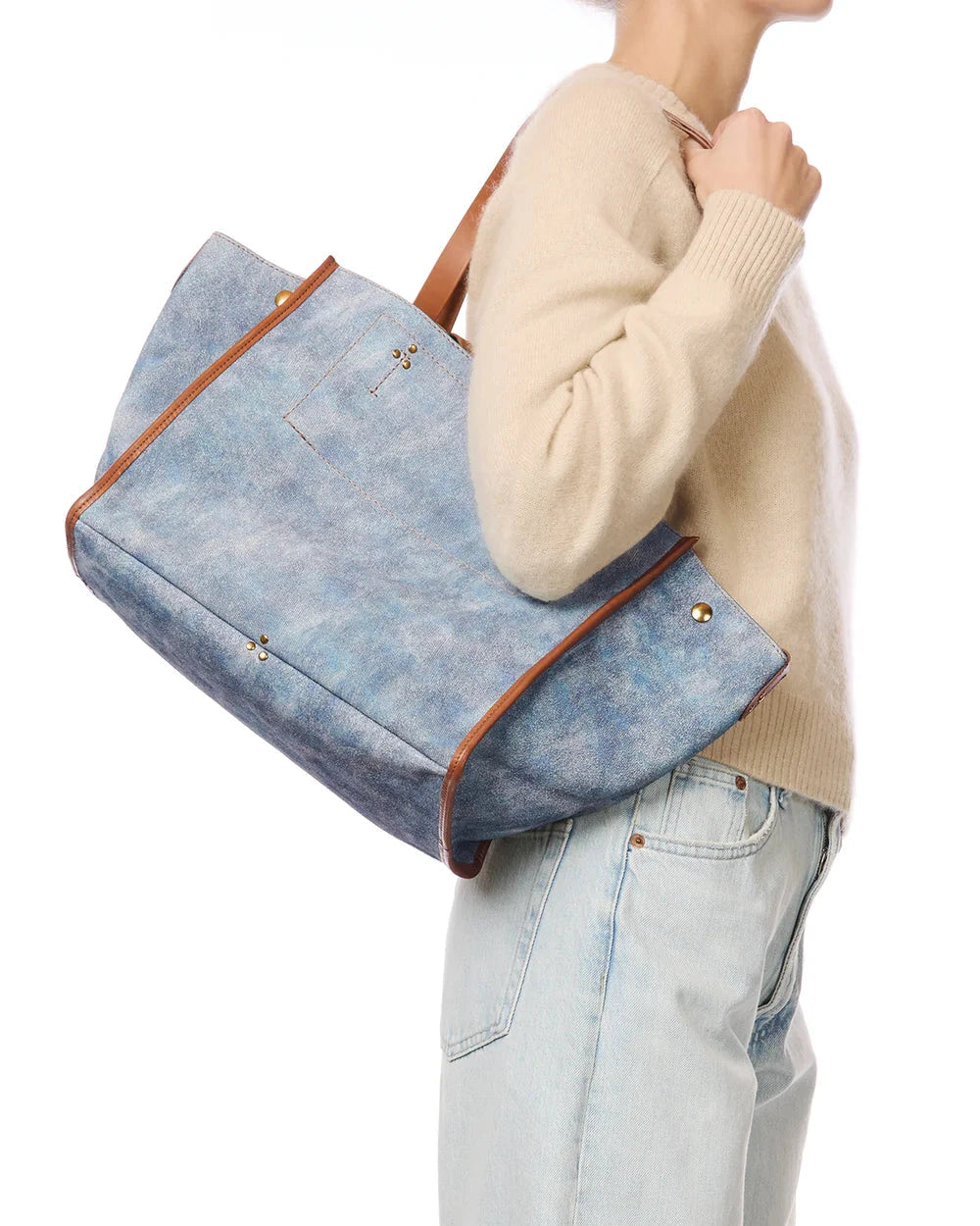 Person holding a blue denim handbag with brown leather accents