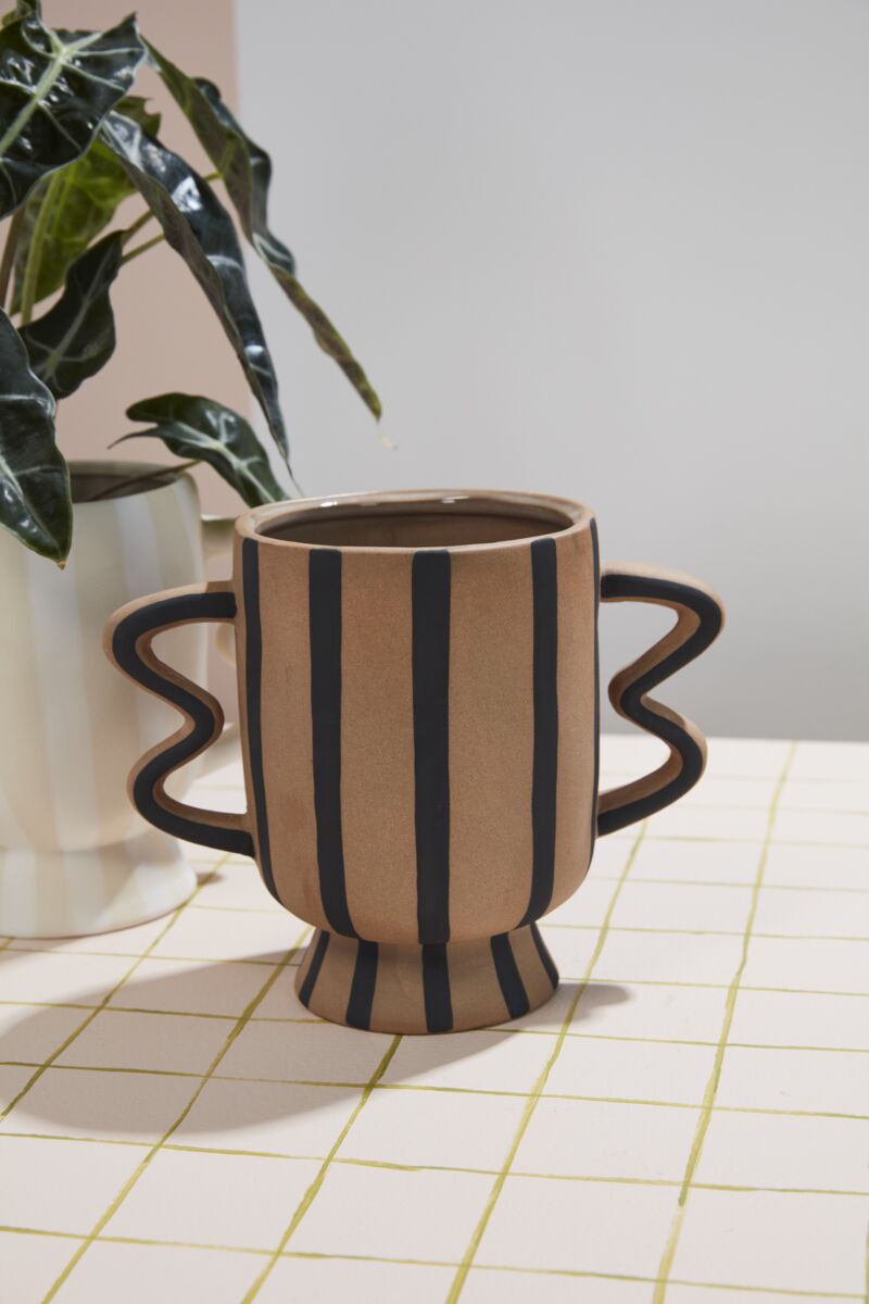 Ceramic cup-shaped vase with striped design on a grid-patterned surface.