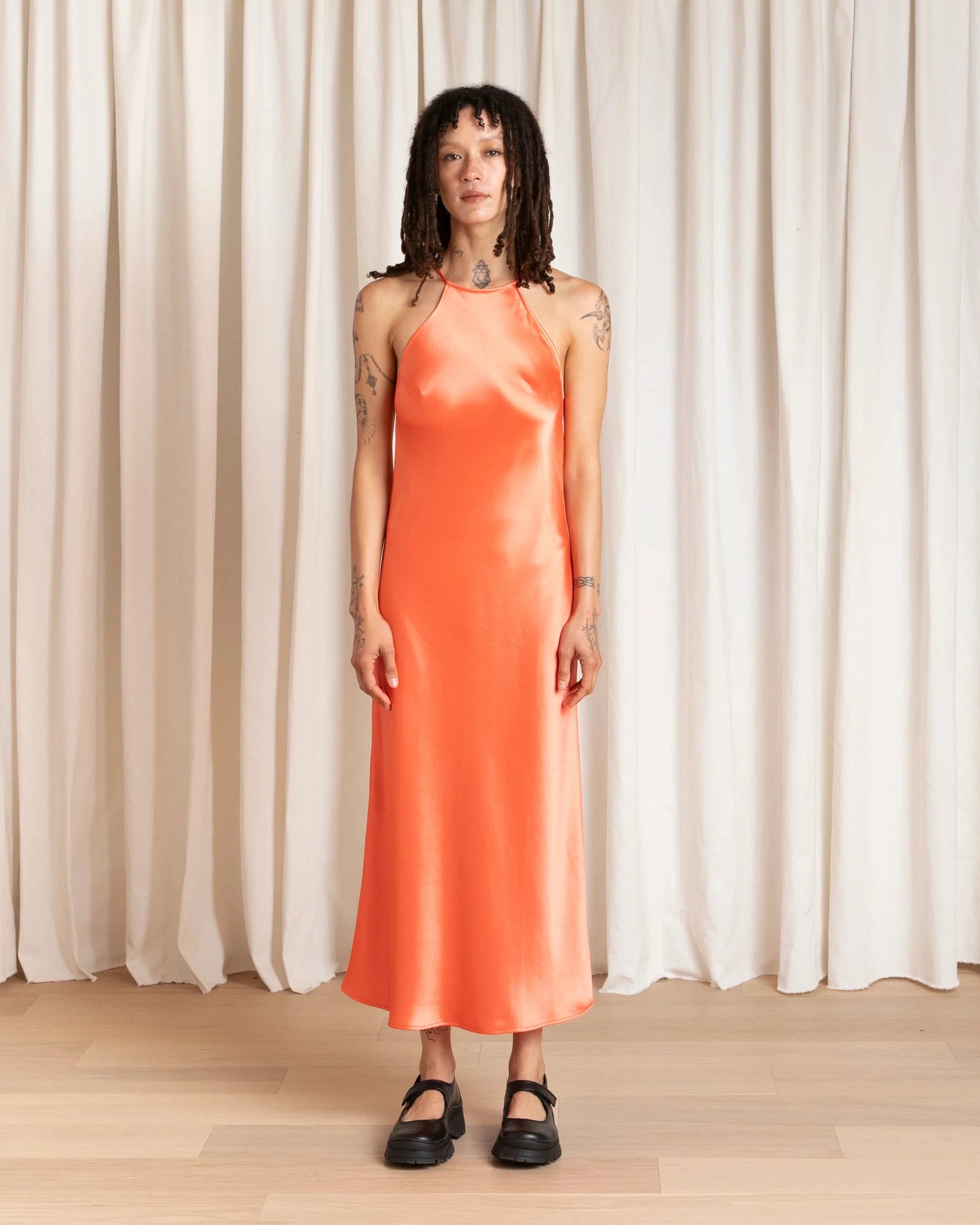 Woman wearing an orange dress standing against a white curtain background