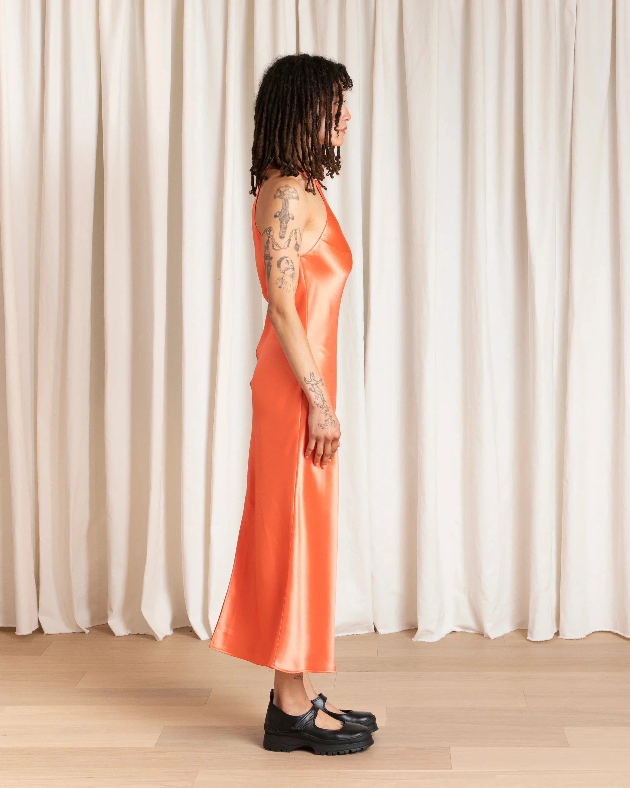 Person wearing an orange dress standing against a white curtain.
