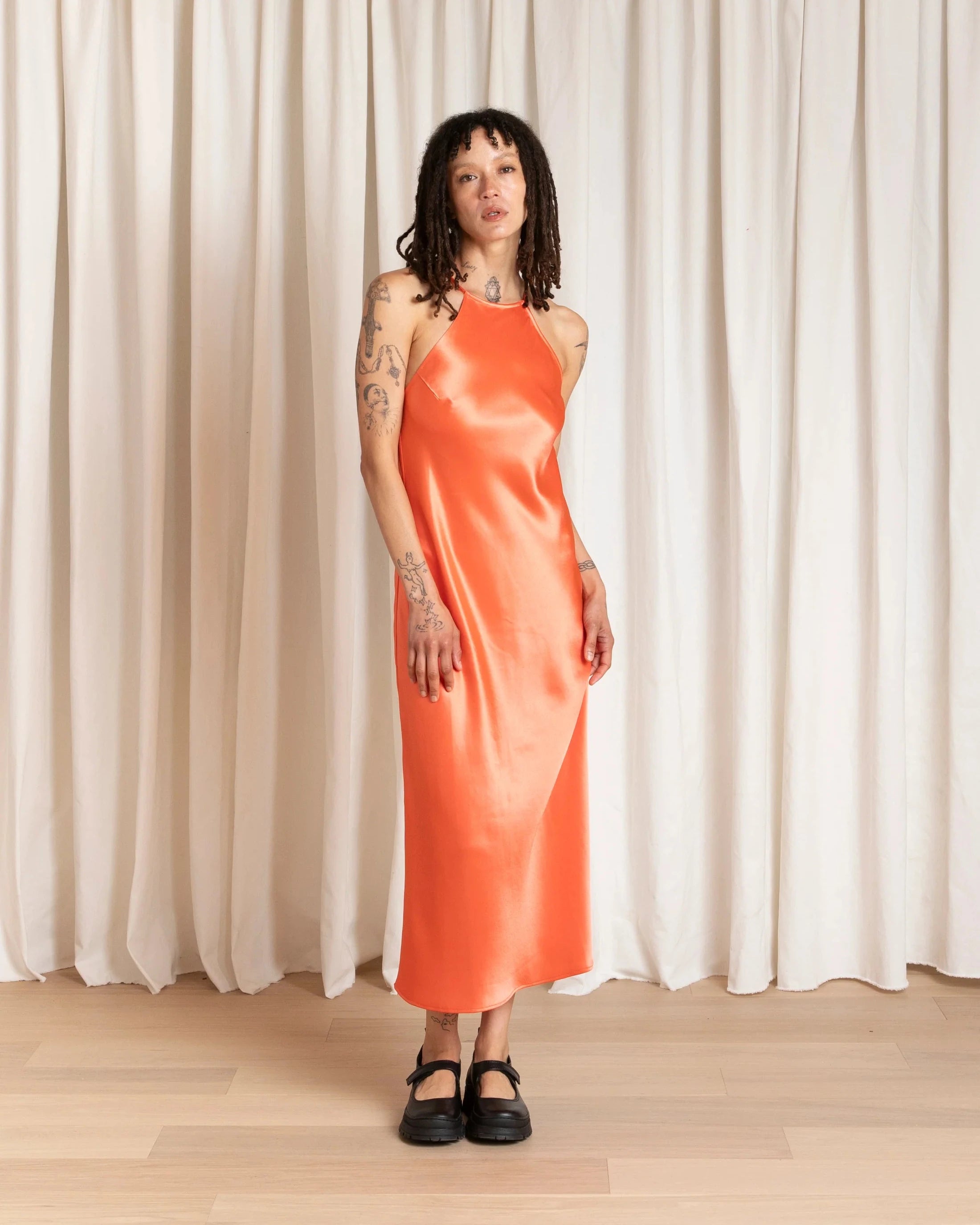 Person wearing an orange dress standing against a white curtain