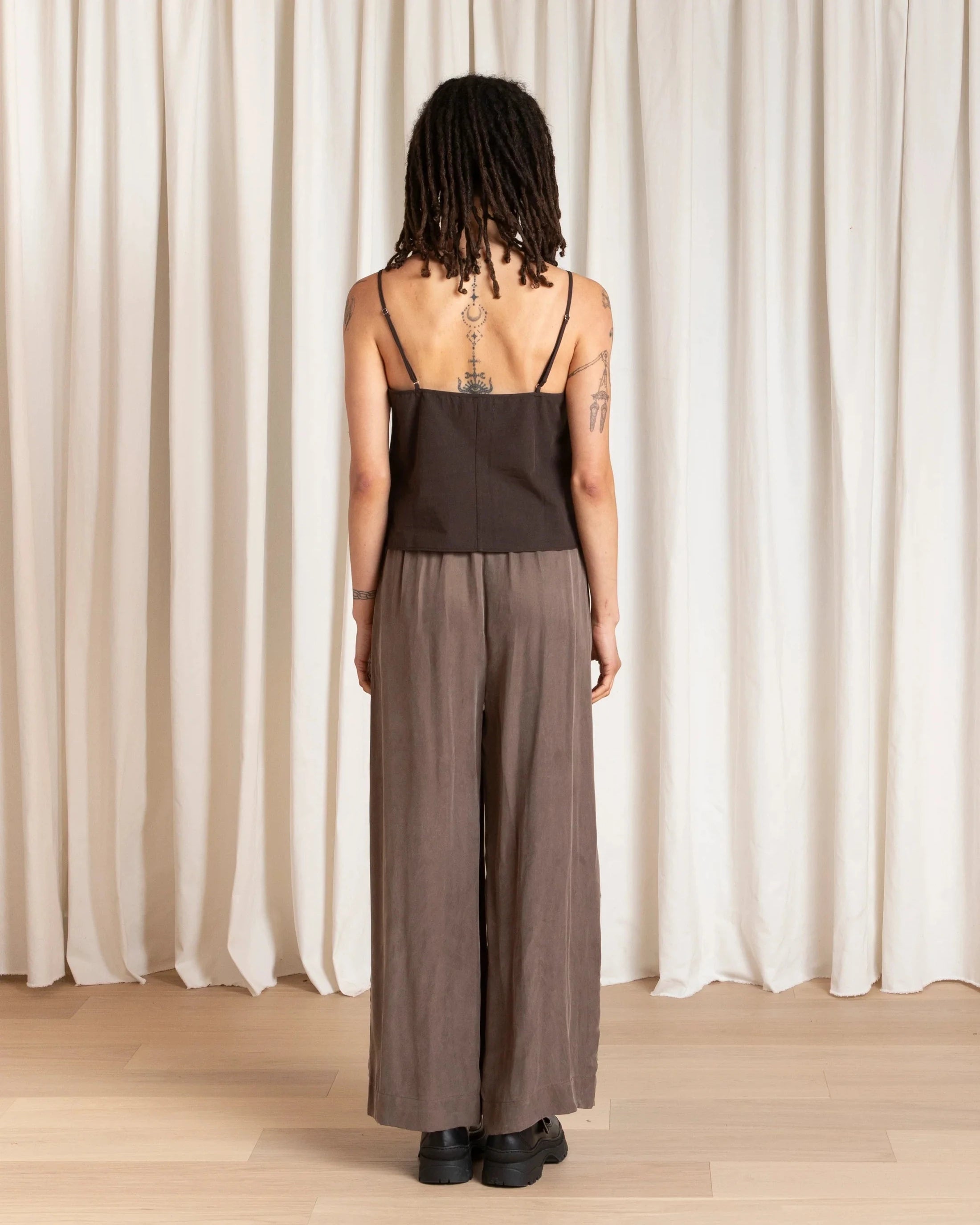 Person wearing a brown jumpsuit standing against a white curtain.