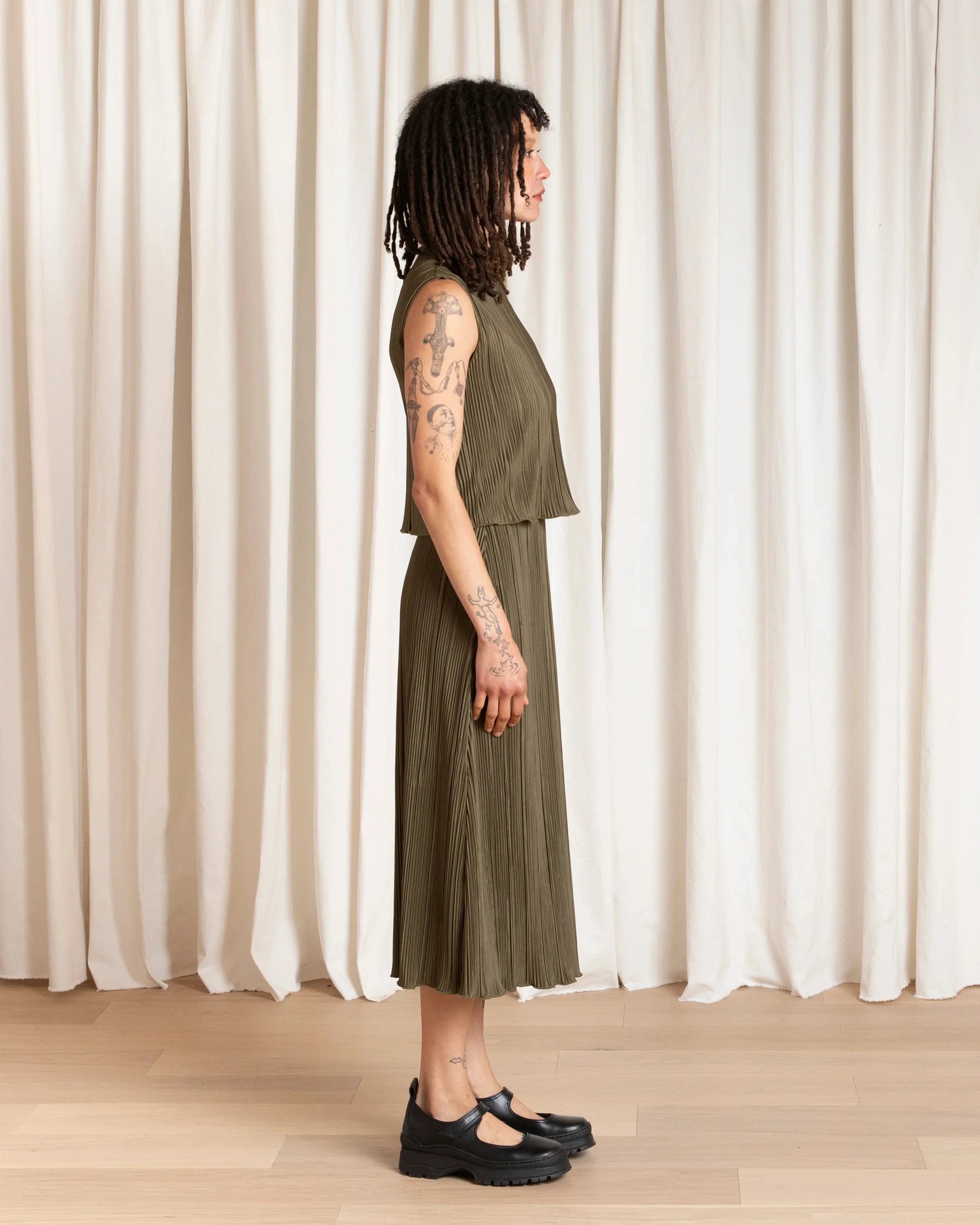 Person wearing a green dress standing against a white curtain.