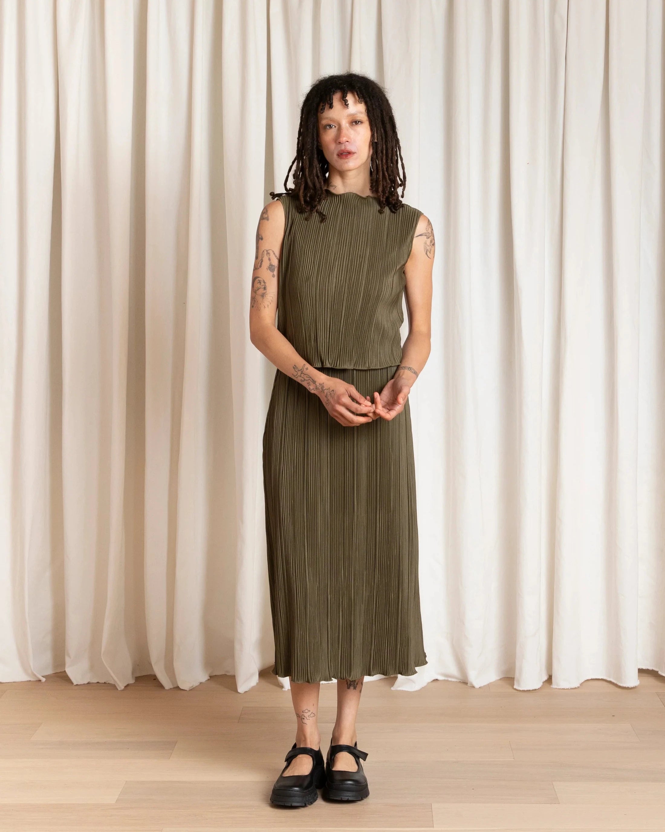 Person wearing a green dress standing in front of white curtains