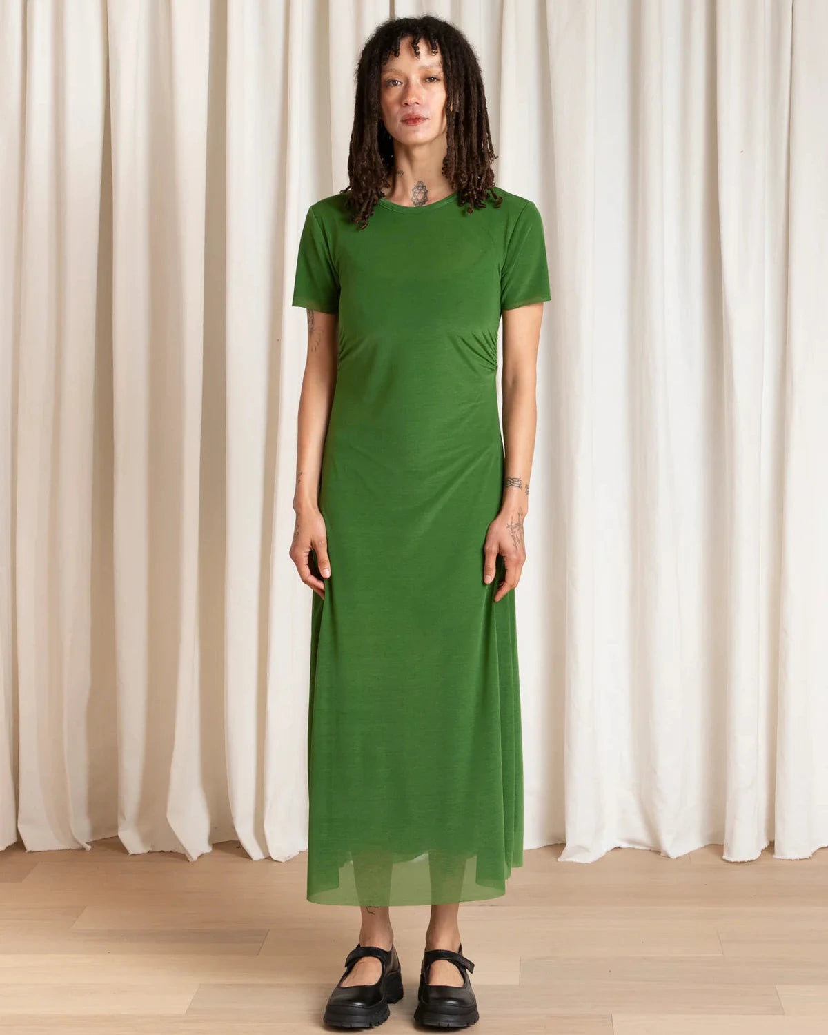 Woman wearing a green dress standing against a white curtain background
