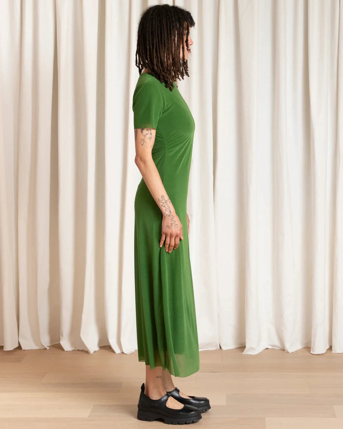 Person wearing a green dress standing against a white curtain.