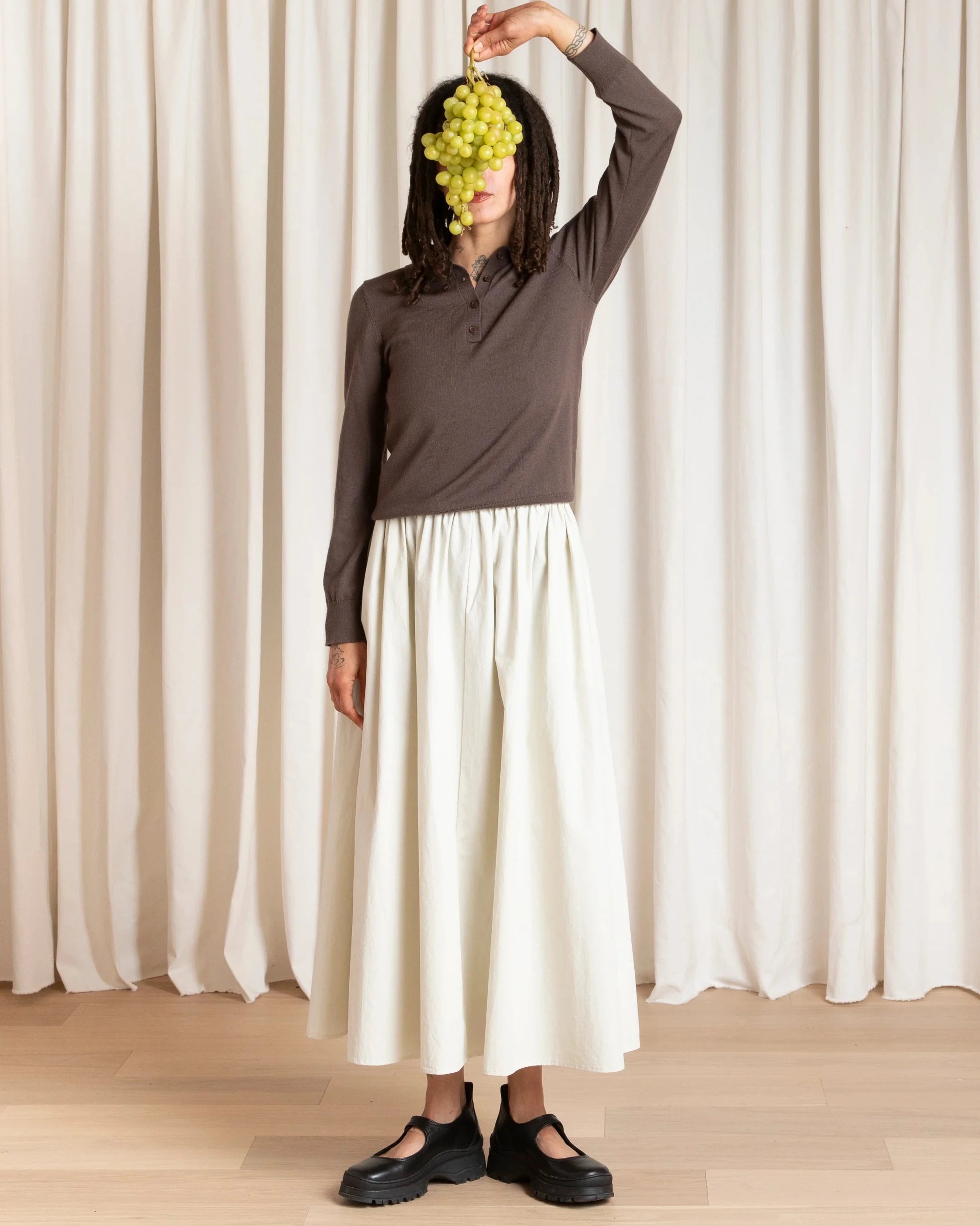 Person holding a bunch of grapes in front of a white curtain