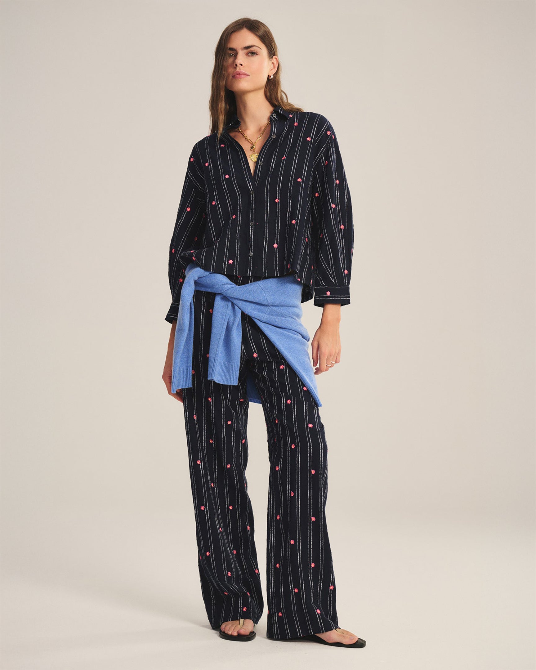 Woman wearing a black patterned shirt and blue scarf with matching pants on a plain background