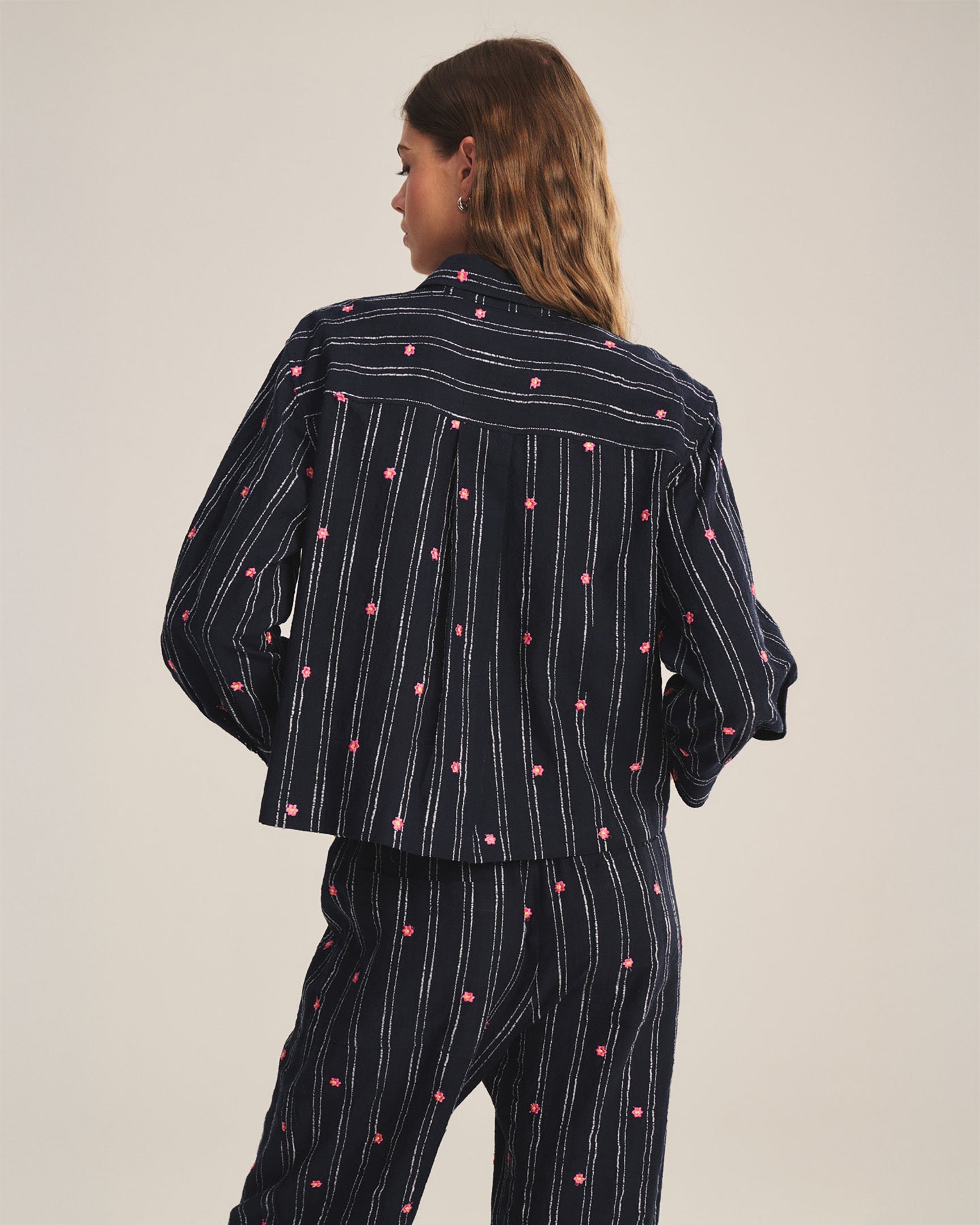 Person wearing a black pinstripe outfit with pink dots on a plain background
