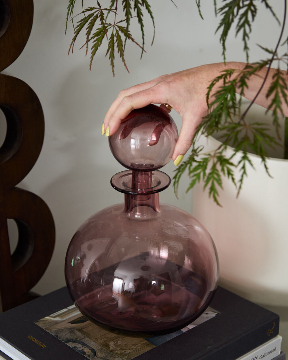 Person holding a purple glass decanter with green leaves in the background