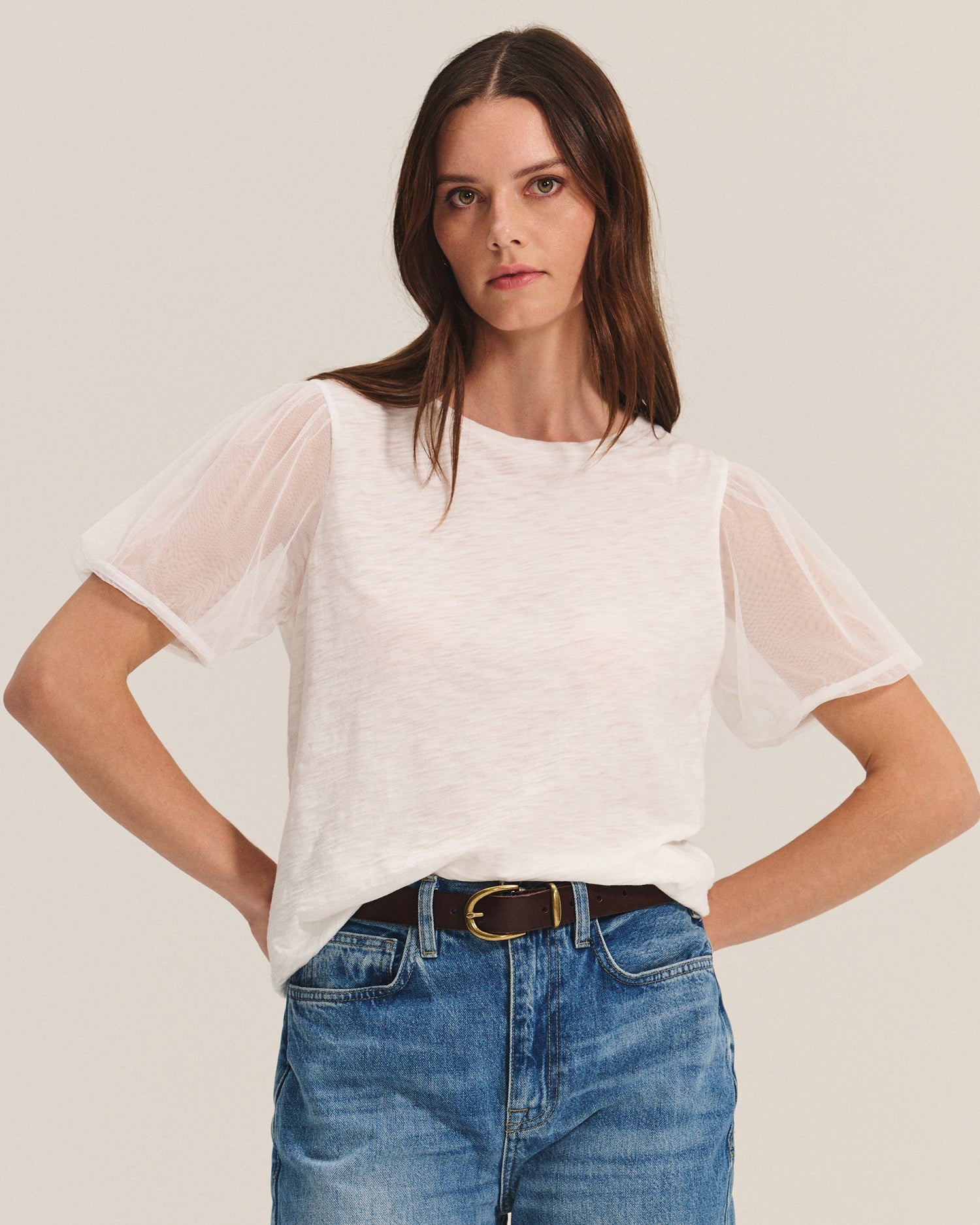 Woman wearing a white sheer top and blue jeans against a plain background