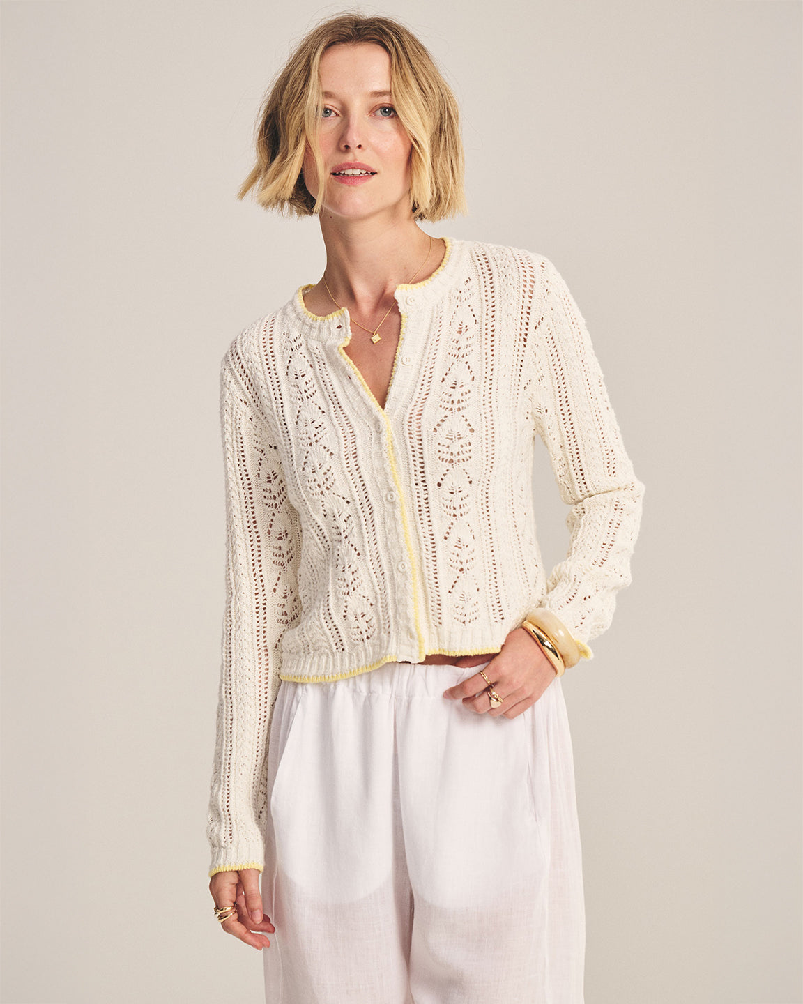 Woman wearing a cream-colored knitted cardigan against a plain background