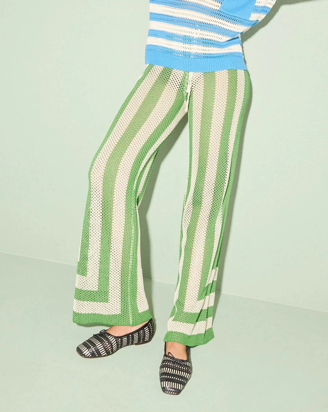 Woman wearing a blue and white striped sweater and green and white striped pants on a light green background