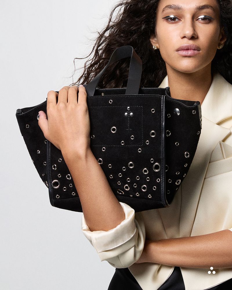 Woman holding a black handbag with decorative elements against a neutral background