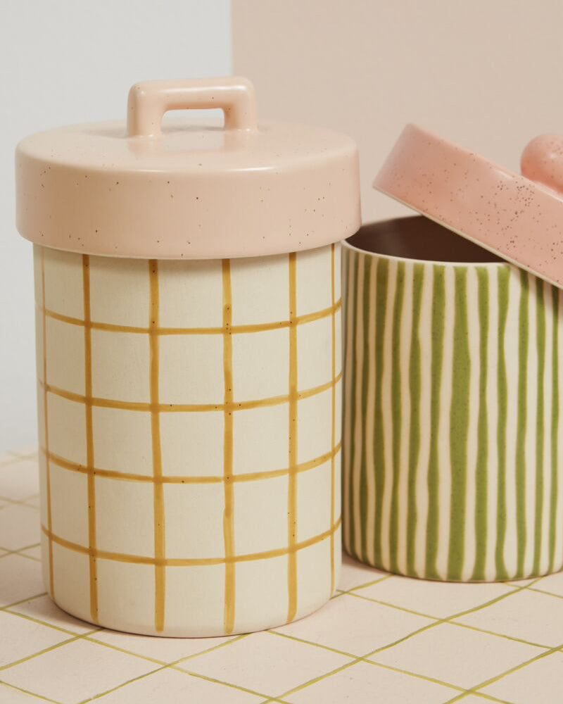 Two ceramic containers with grid and stripe patterns on a tiled surface