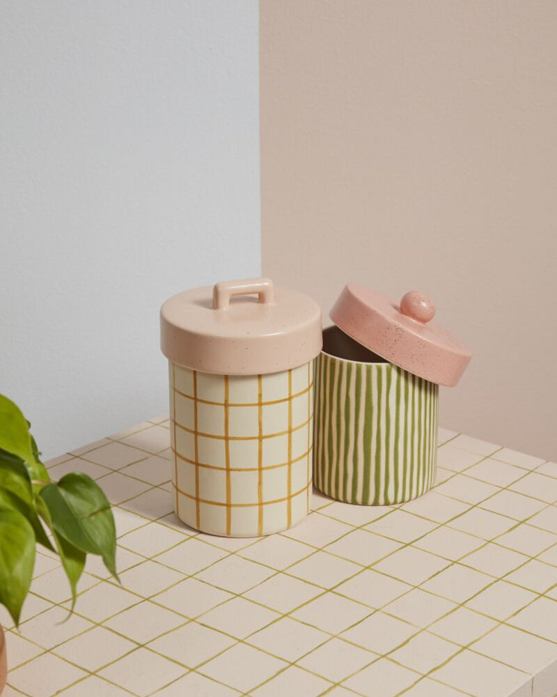 Two cylindrical storage containers with pink lids on a tiled surface.