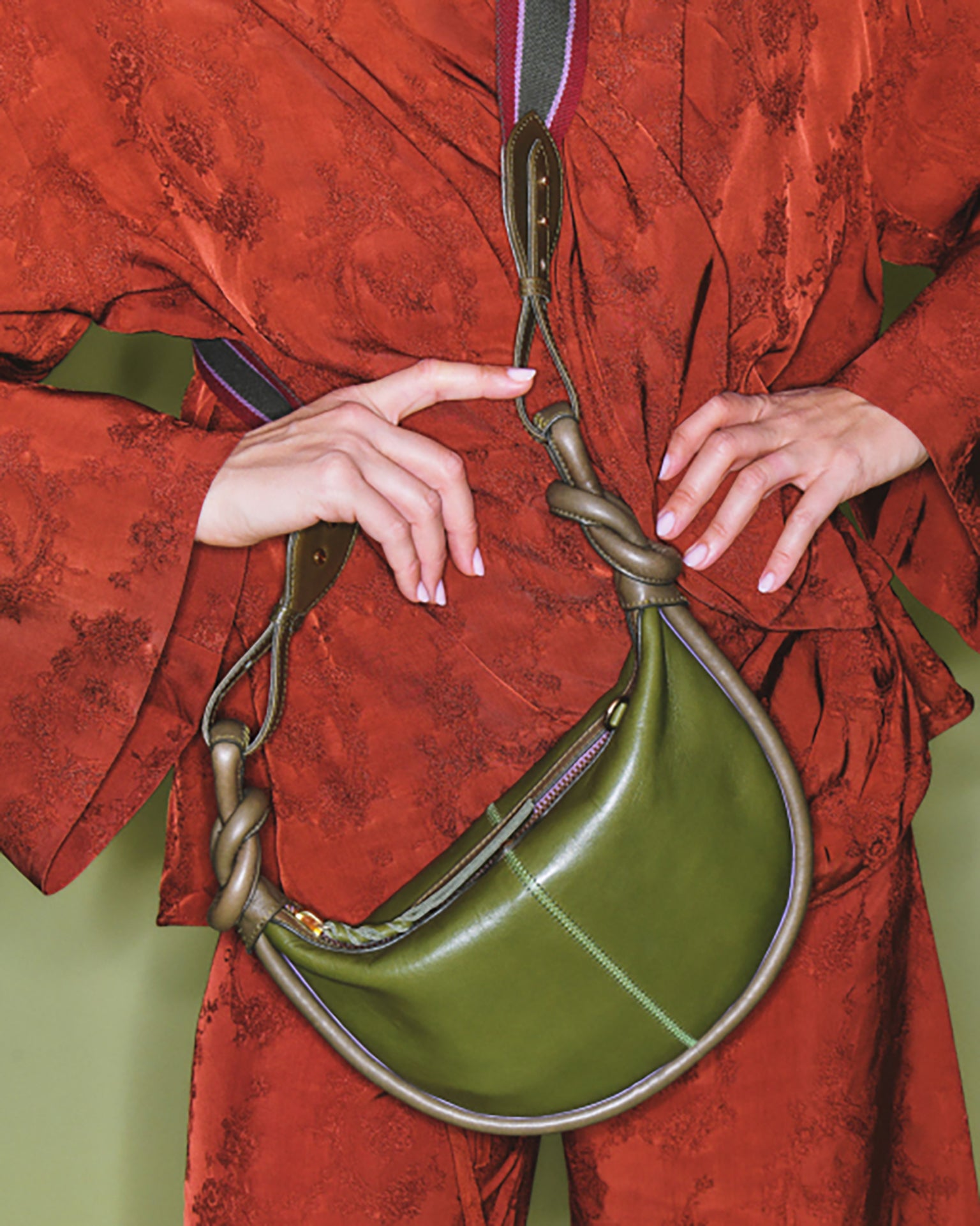 Green handbag with gold accents held by a person wearing a red outfit.