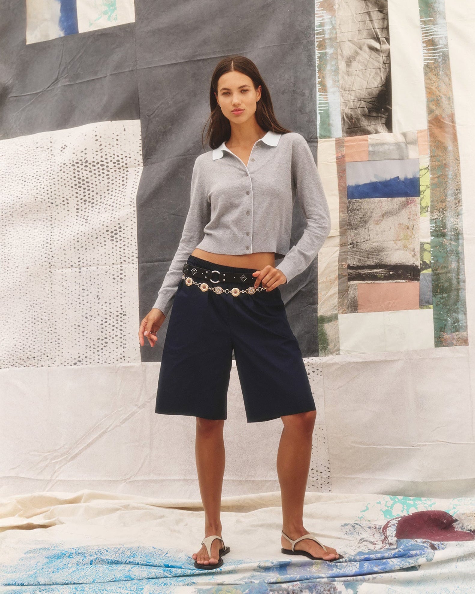 Woman wearing a light gray shirt and black shorts standing in front of a textured wall with abstract patterns.