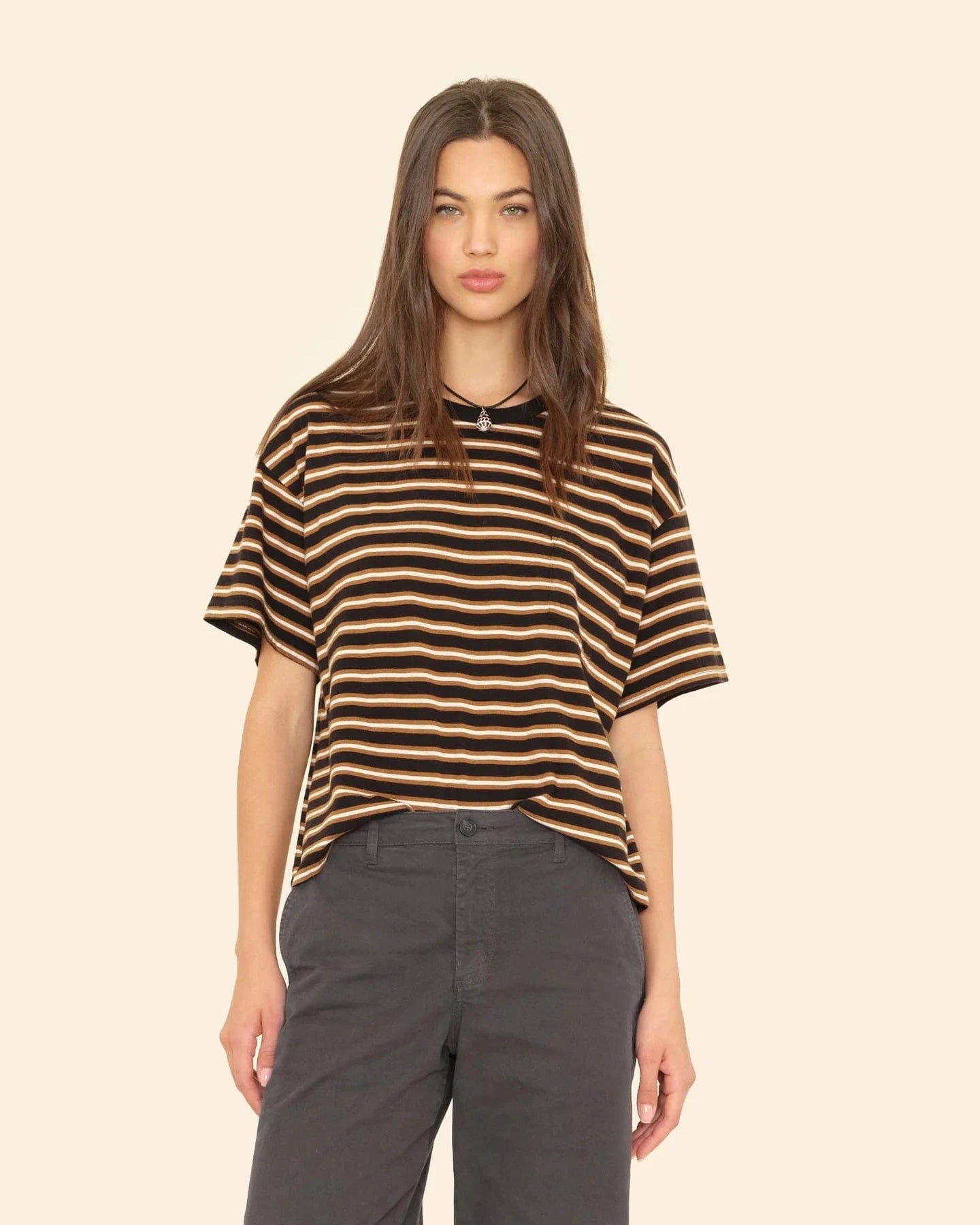 Woman wearing a black and brown striped shirt with gray pants on a beige background