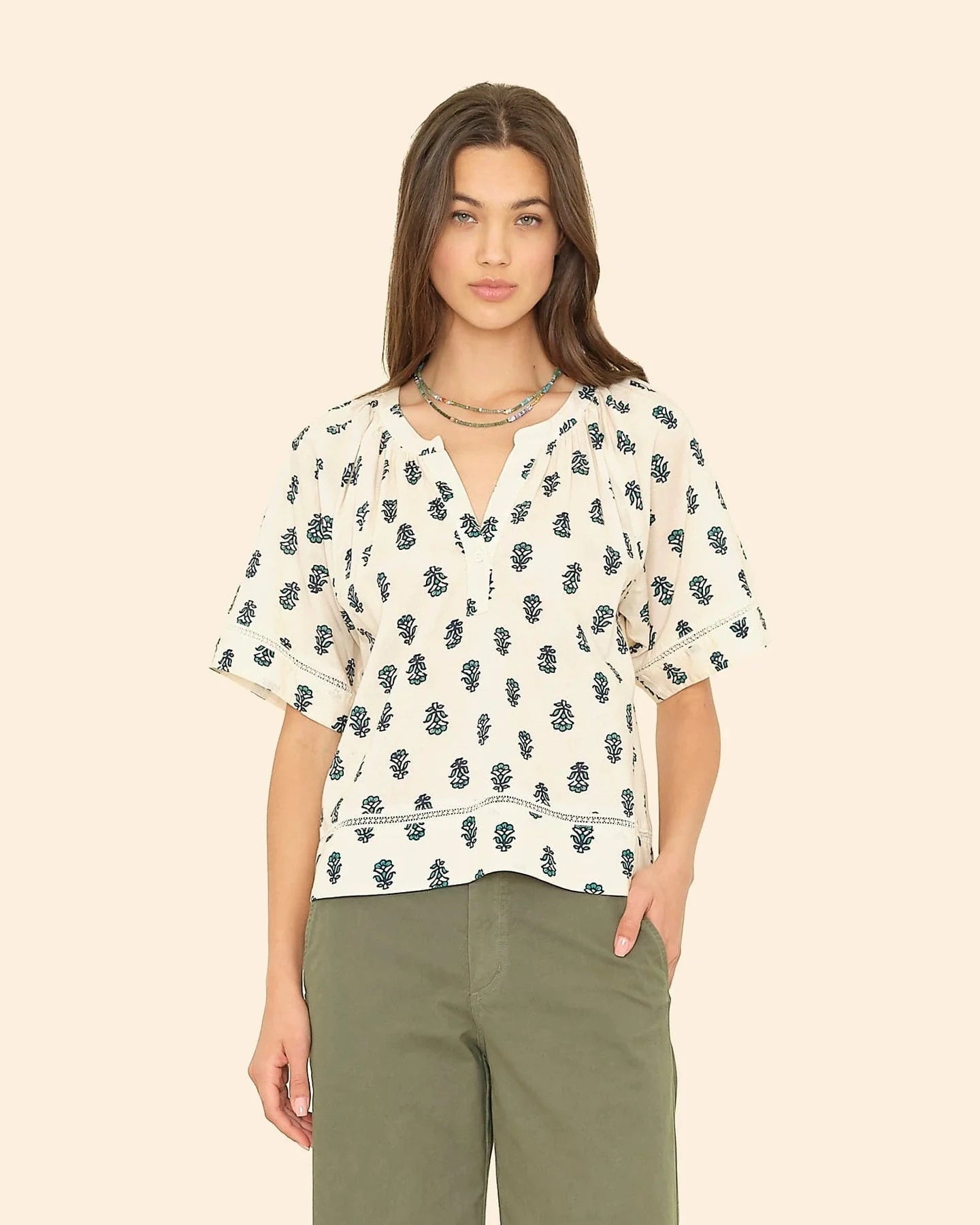 Woman wearing a patterned blouse and green pants on a beige background