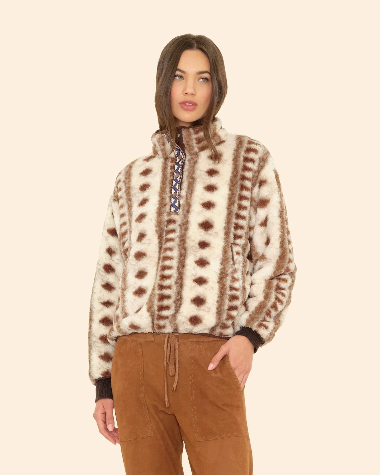 Person wearing a patterned sweater and brown pants on a beige background