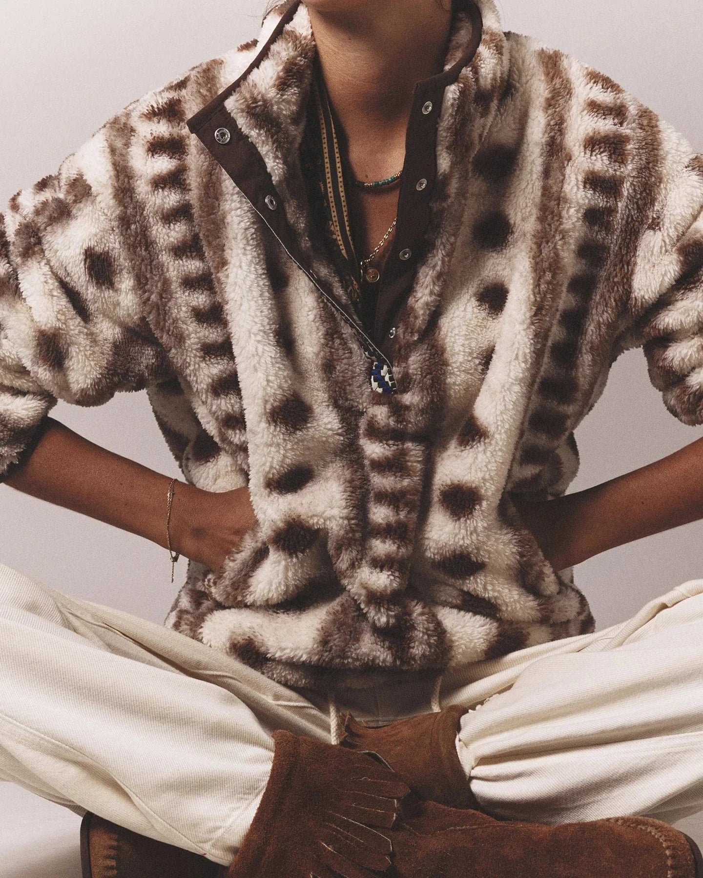 Person wearing a patterned sweater and white pants with brown shoes on a neutral background