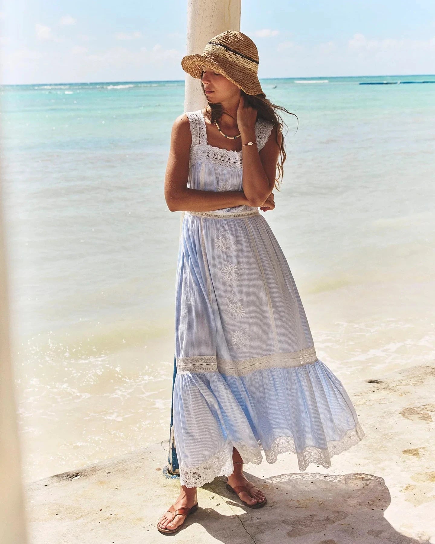 Woman in a white dress and straw hat standing on a beach.