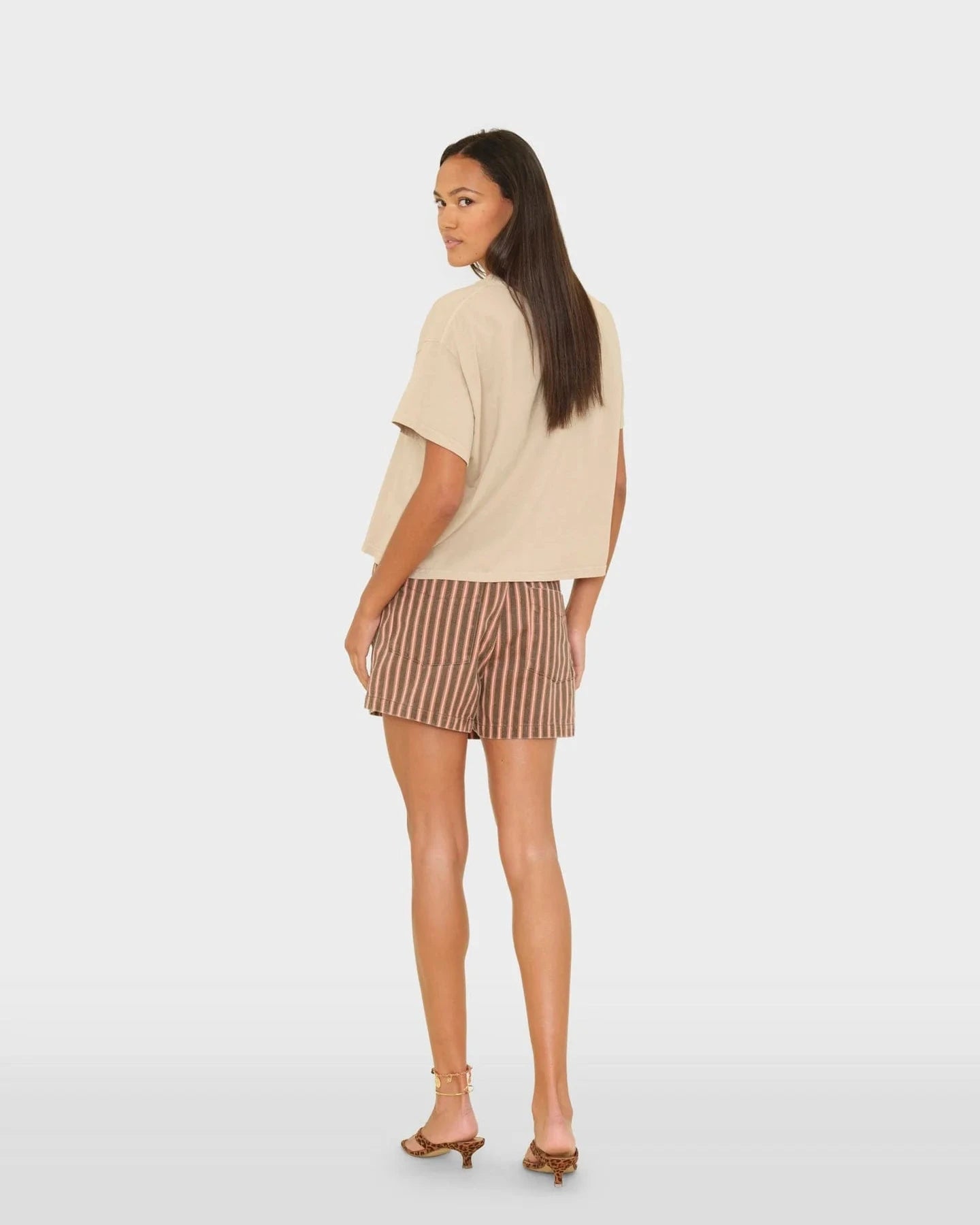 Woman wearing a beige top and striped shorts on a white background