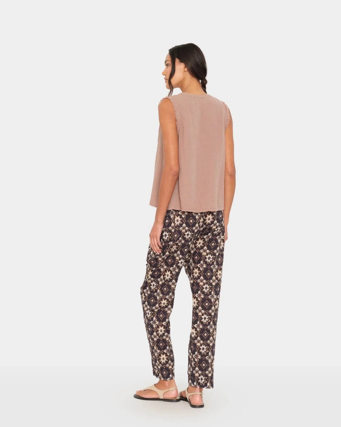Woman wearing a beige sleeveless top and floral pants on a white background