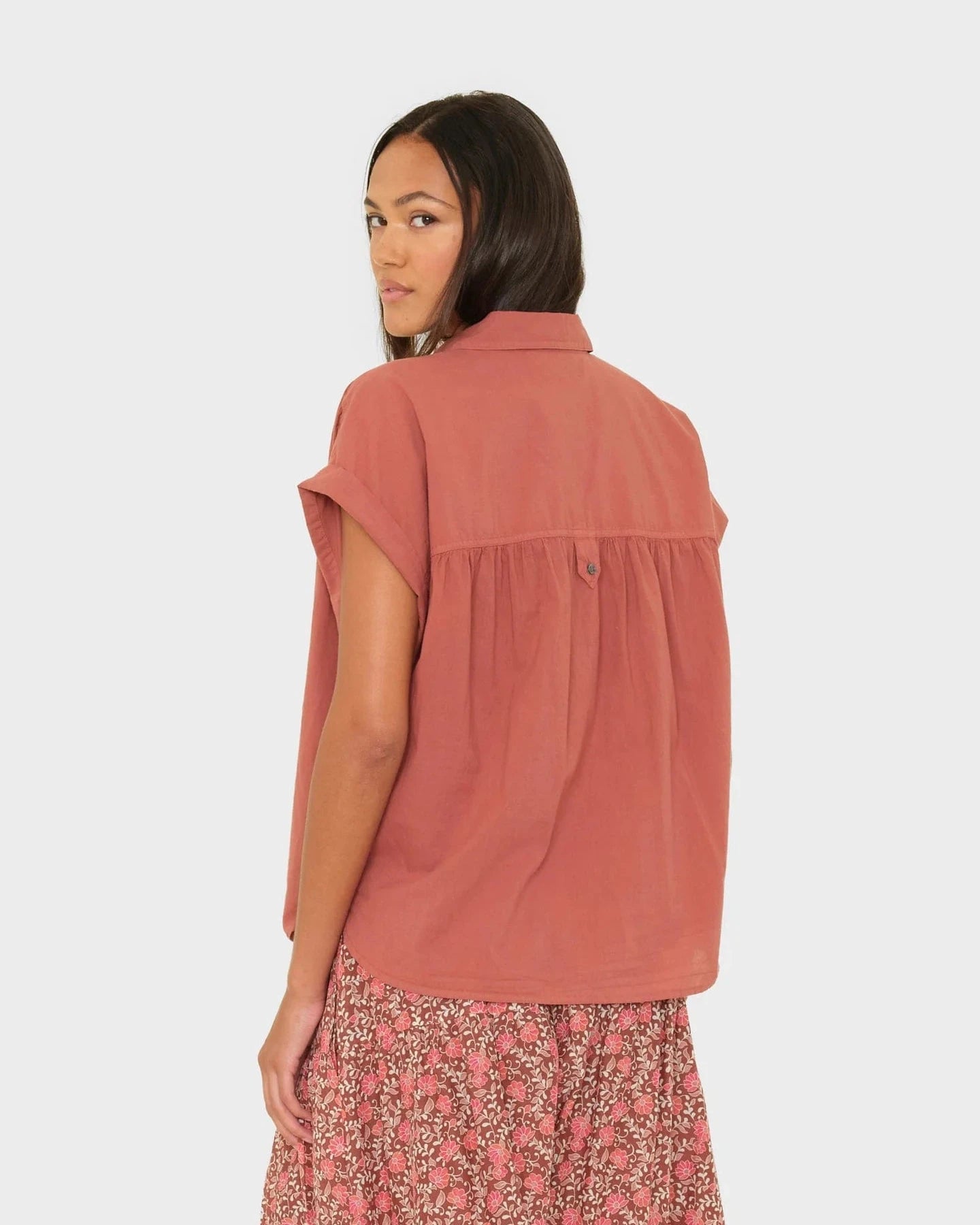 Woman wearing a rust-colored sleeveless top with a plain background