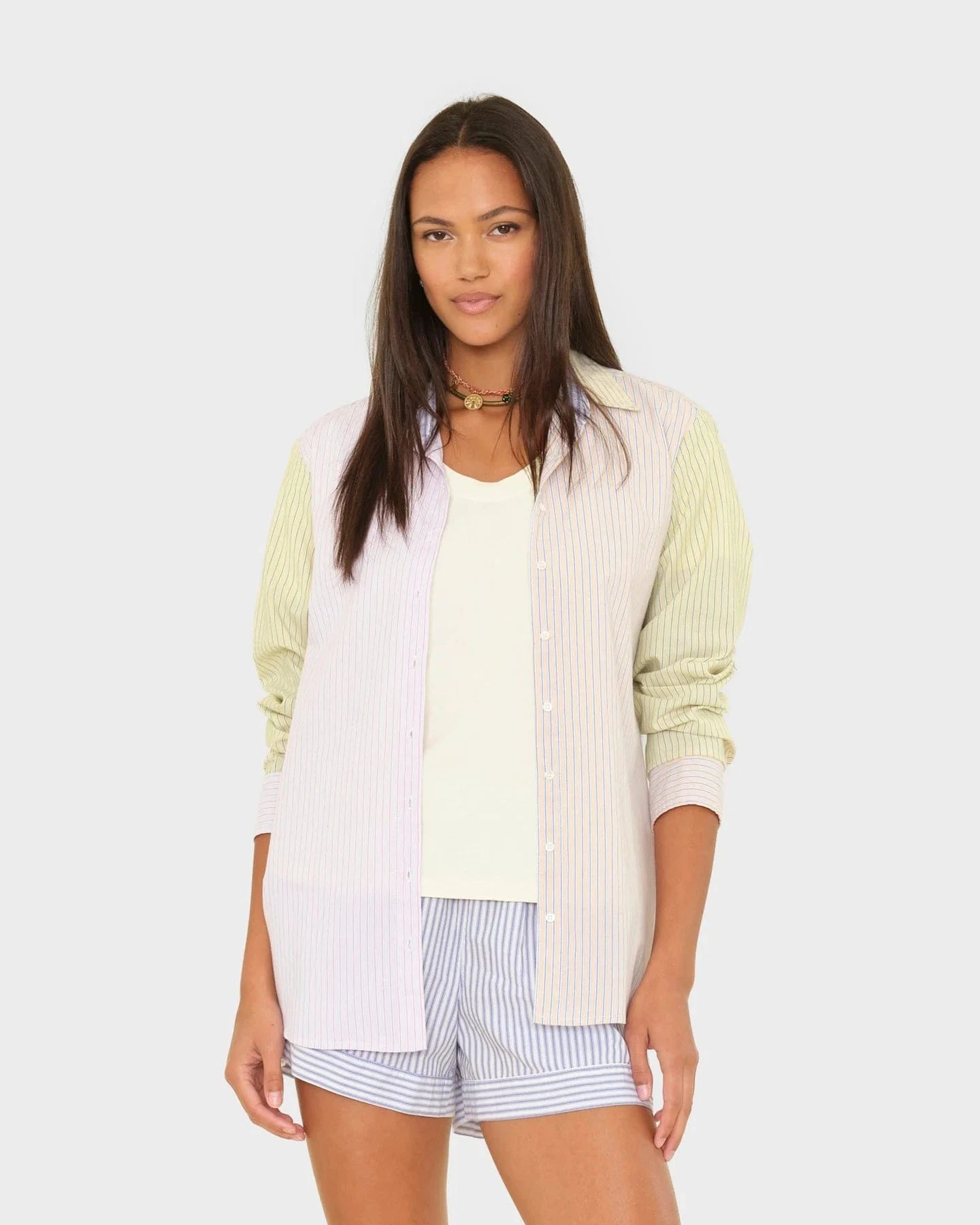 Woman wearing a light green cardigan over a white shirt and striped shorts on a white background