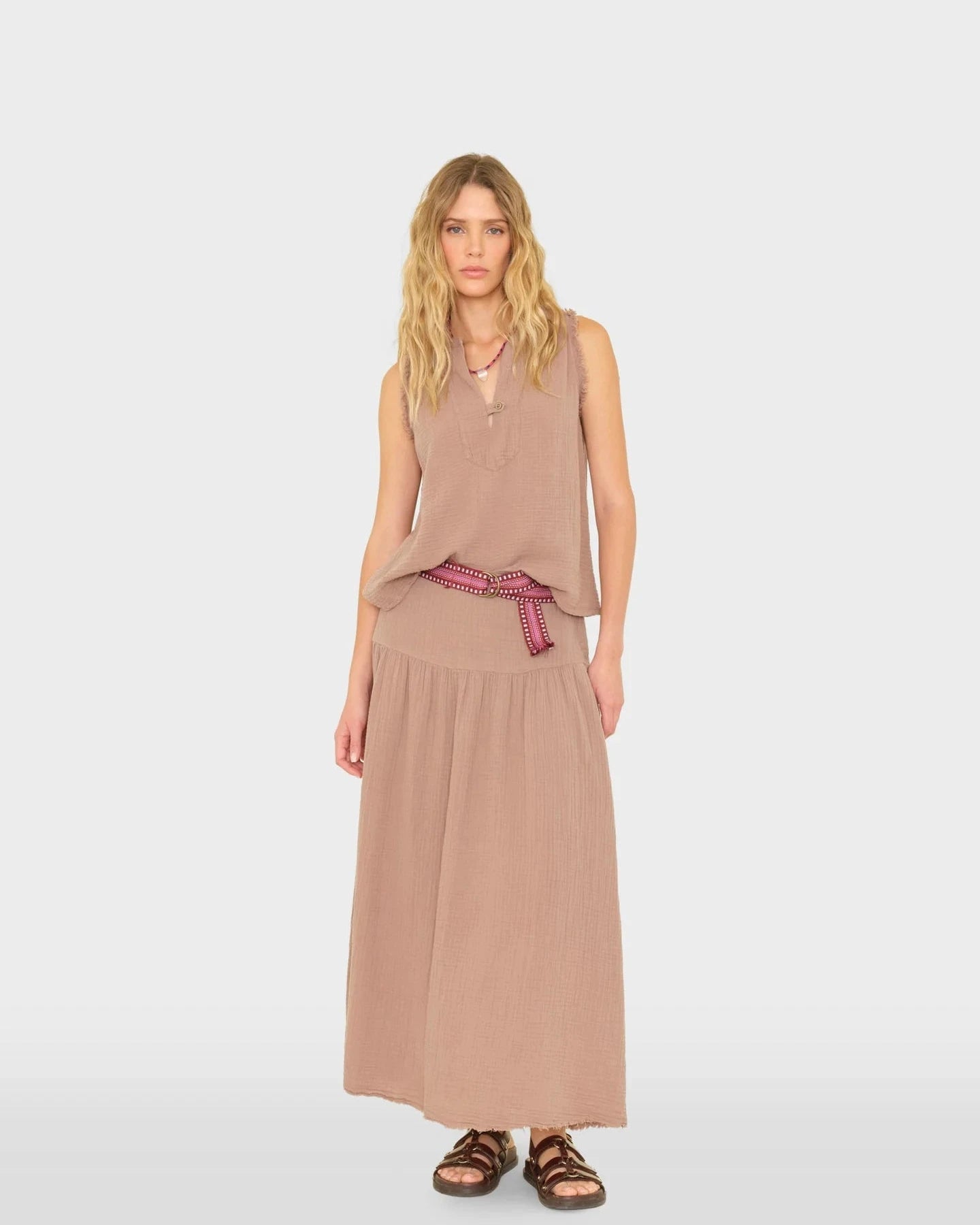Woman wearing a beige sleeveless top and long skirt with a red belt on a white background