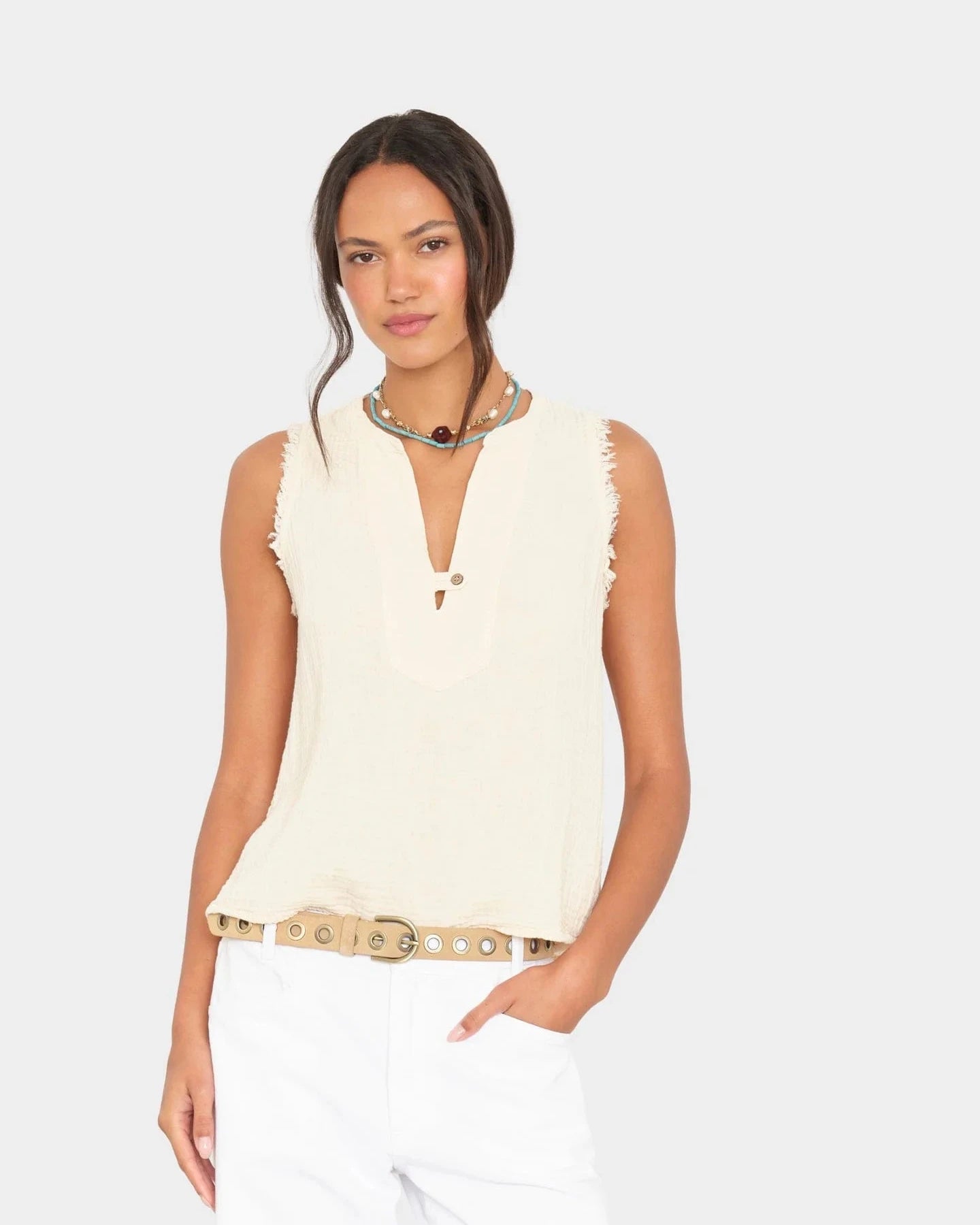 Woman wearing a cream sleeveless top with fringe details on a white background