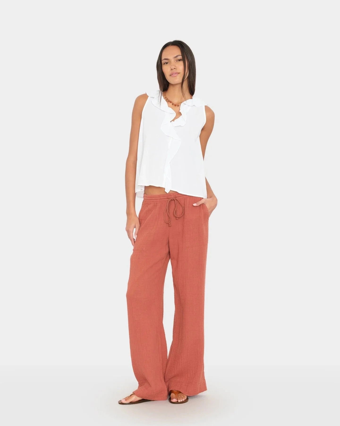 Woman wearing a white sleeveless top and rust-colored pants on a white background