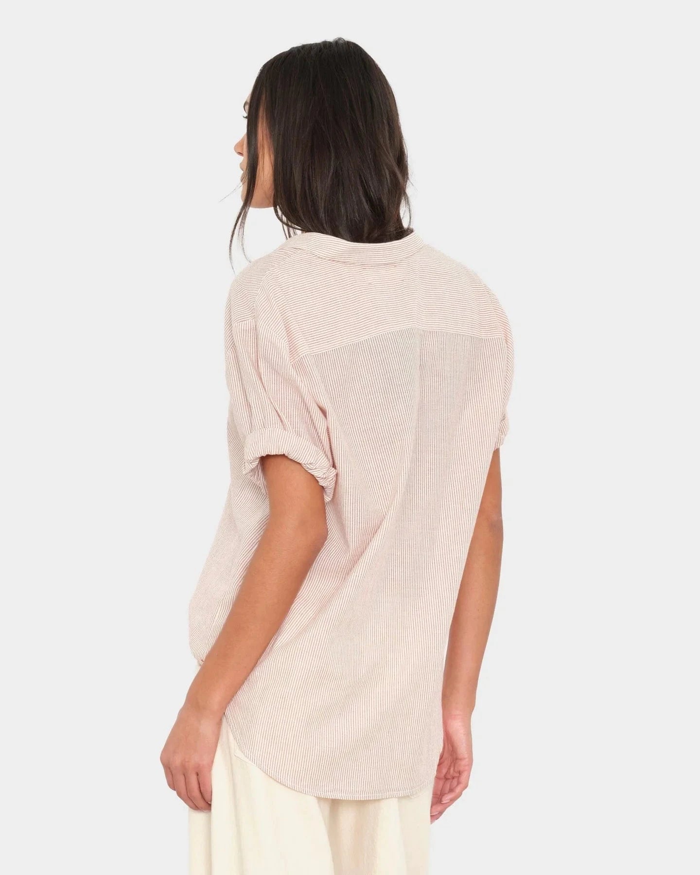 Woman wearing a light beige shirt and white pants on a plain background