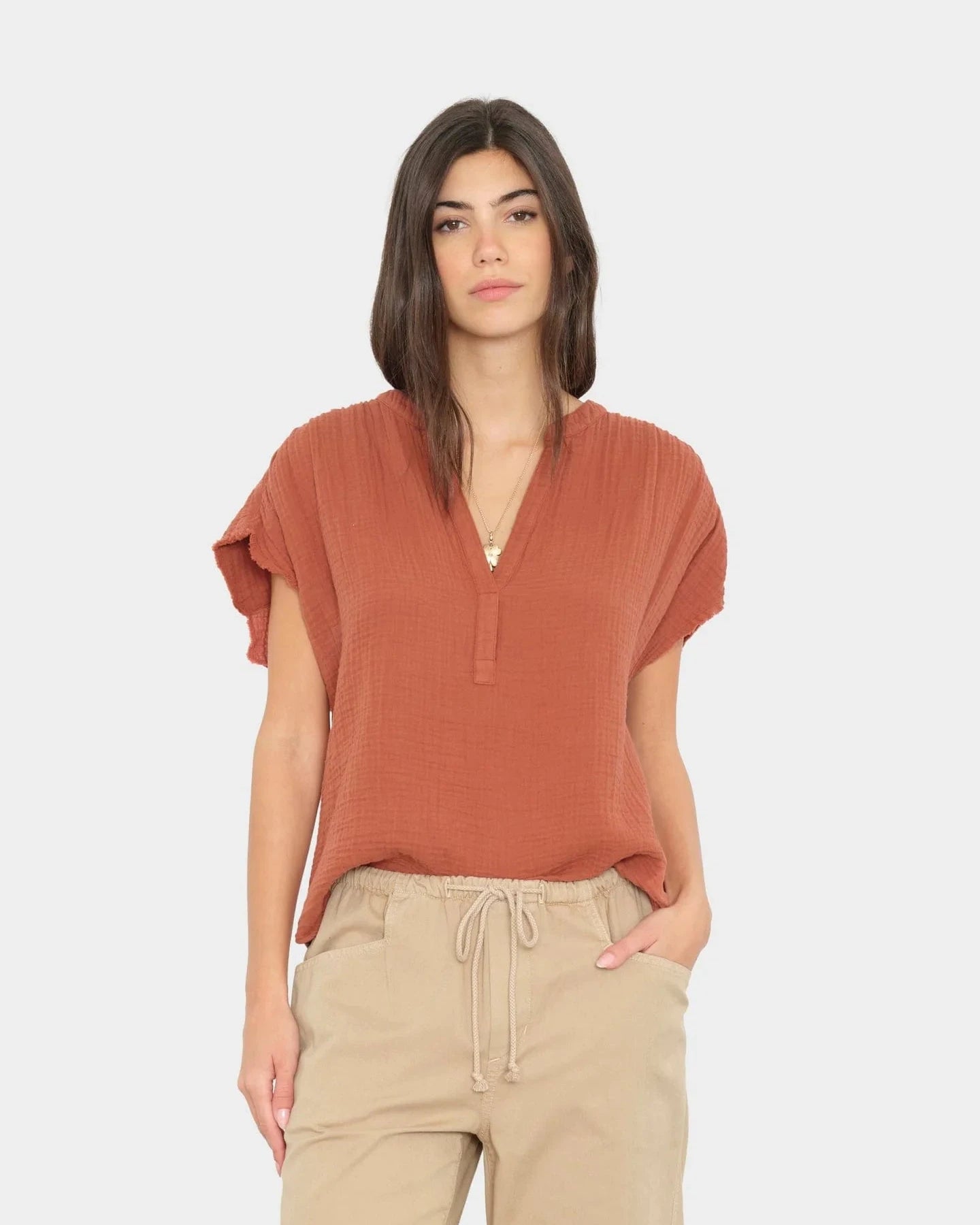 Woman wearing a rust-colored short-sleeve top and beige pants on a white background