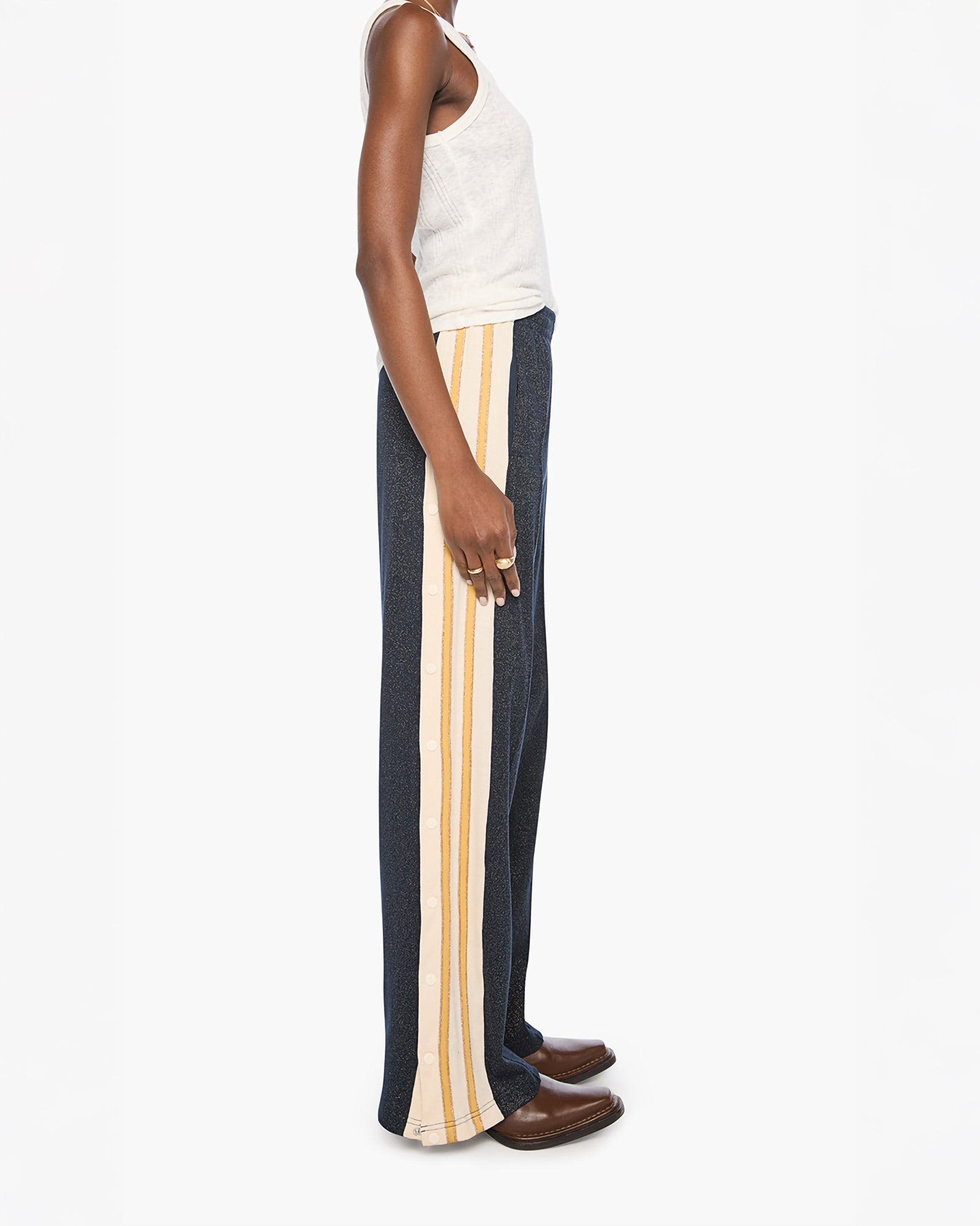 A side-profile view of a model wearing dark navy wide-leg trousers with a vertical cream stripe down the side, styled with a white tank top and brown leather loafers against a plain white background.