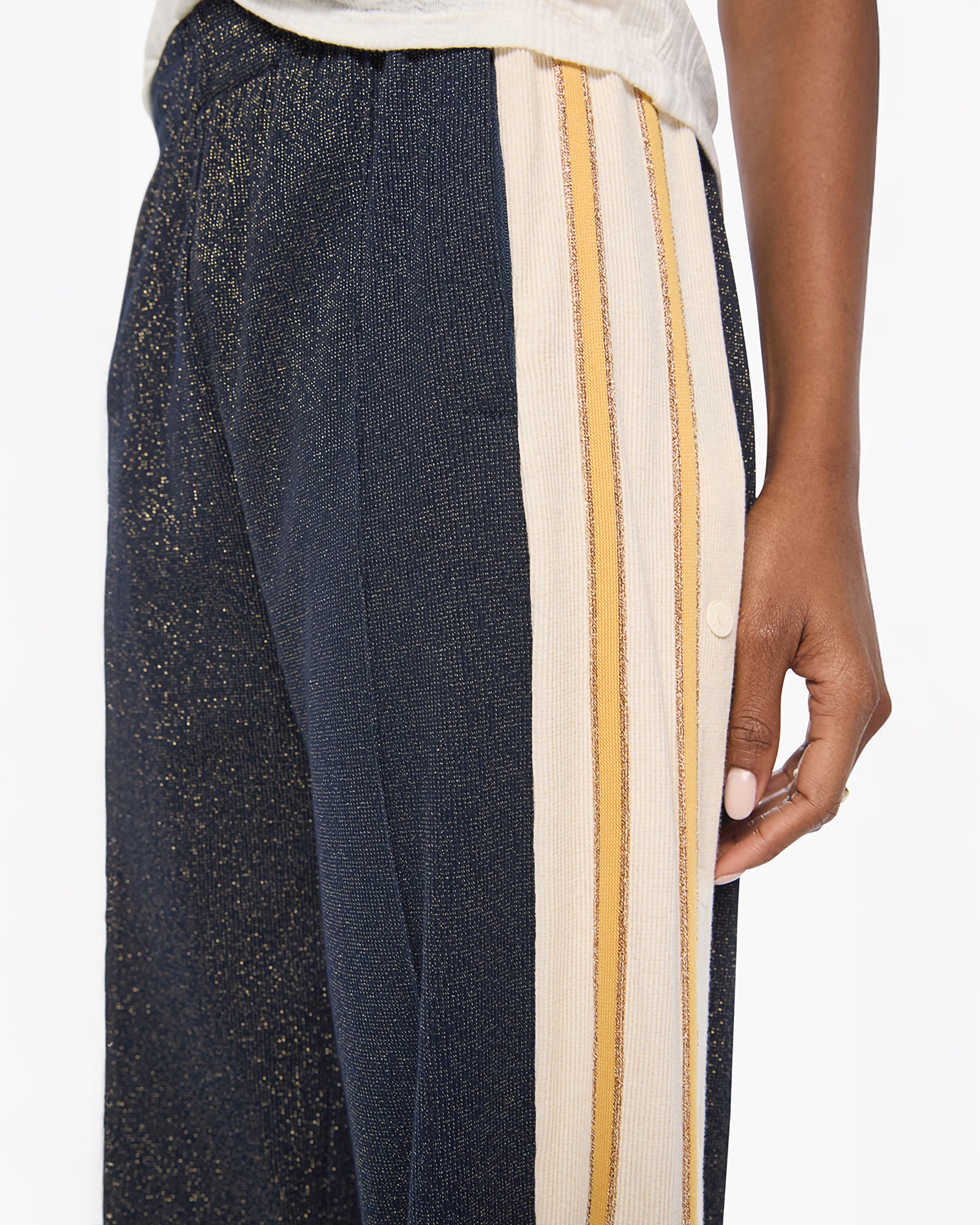 Close-up of a person wearing wide-leg trousers with a navy base, subtle gold speckling, and two vertical cream and mustard yellow stripe panels on the side.