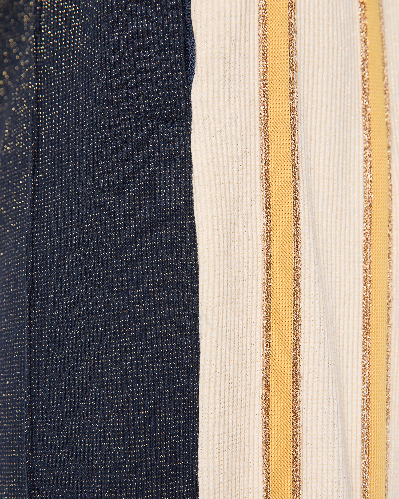 Close-up of a striped knit fabric with vertical panels in dark navy blue, off-white, and mustard yellow with shimmering gold glitter-like stripes.