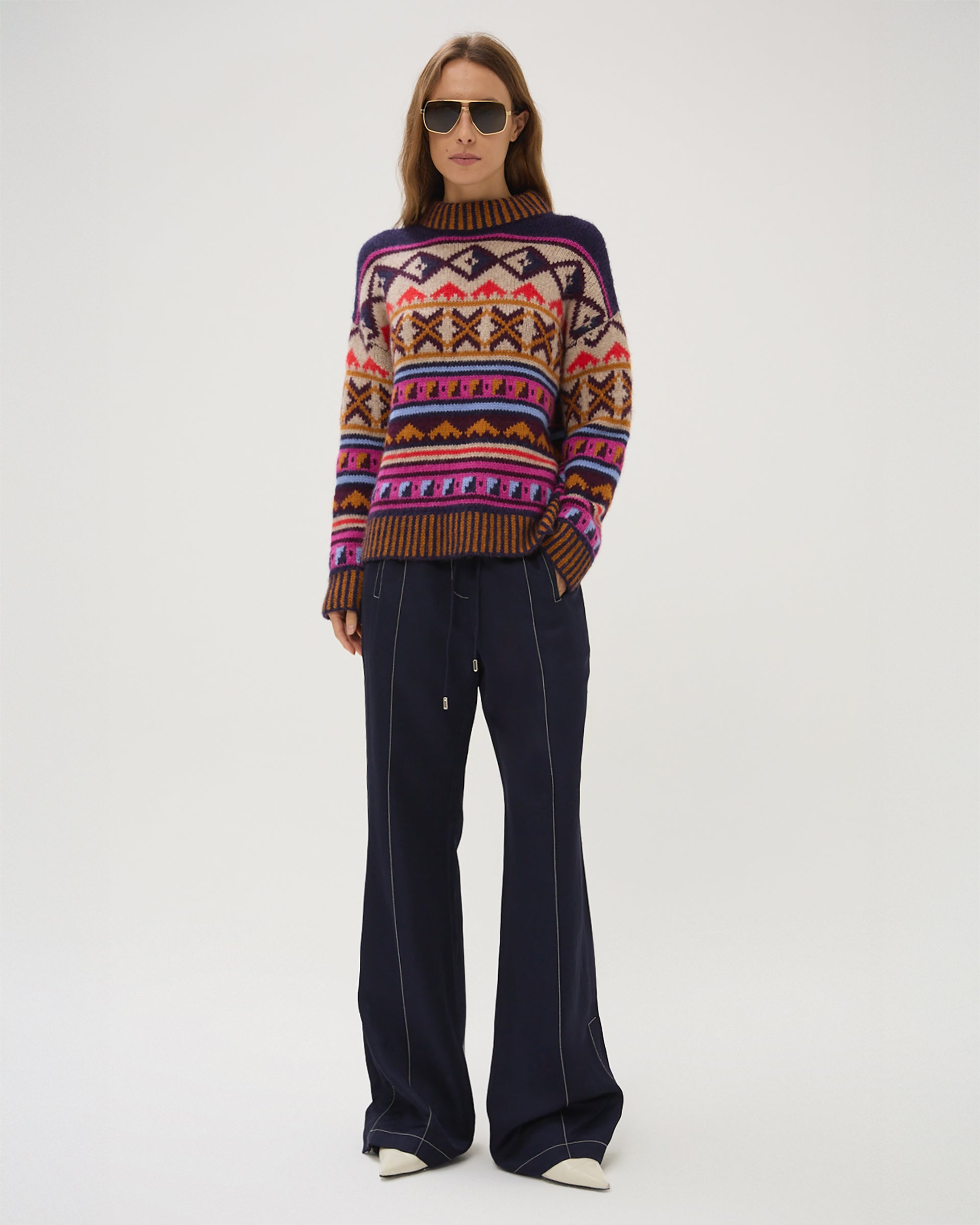 Person wearing a patterned sweater and dark pants on a white background