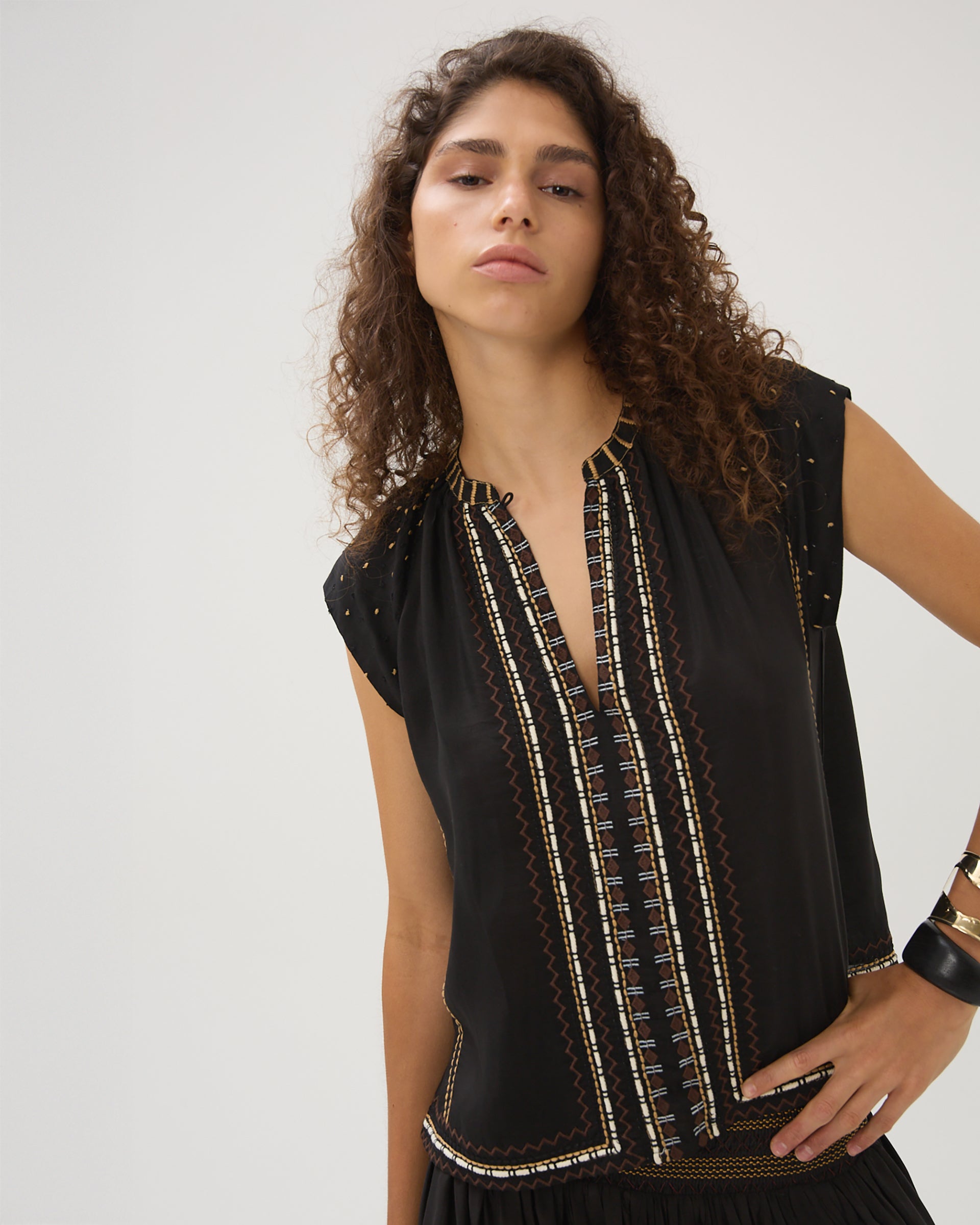 Woman wearing a black sleeveless top with intricate patterns on a white background