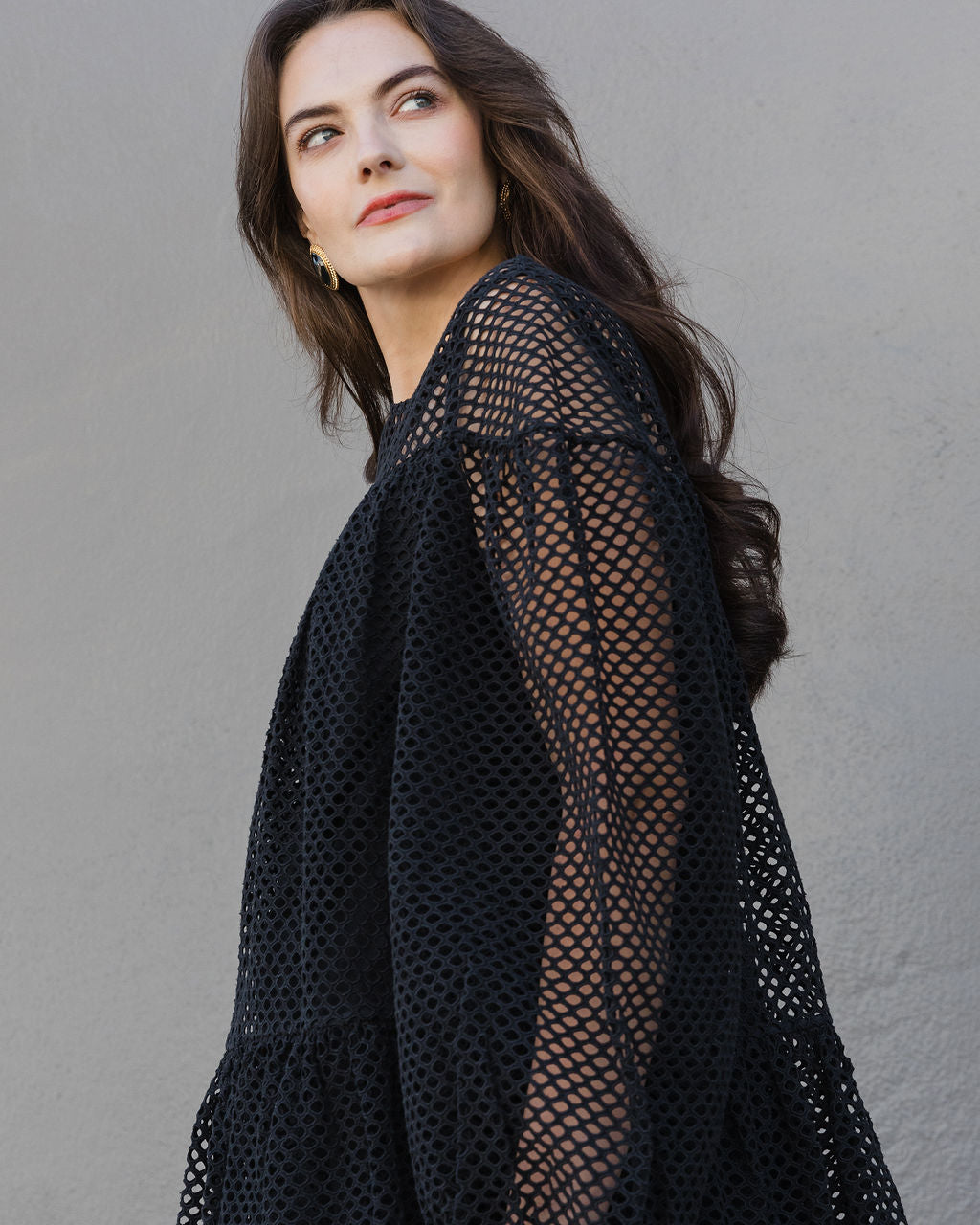 Woman wearing a black mesh dress against a gray background