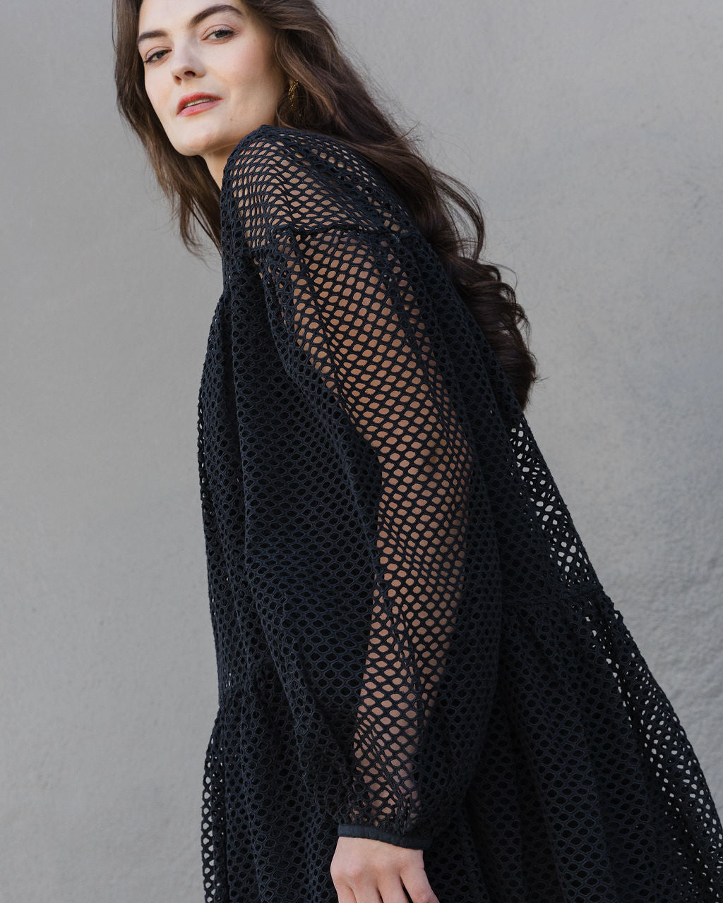 Woman wearing a black fishnet top against a gray background