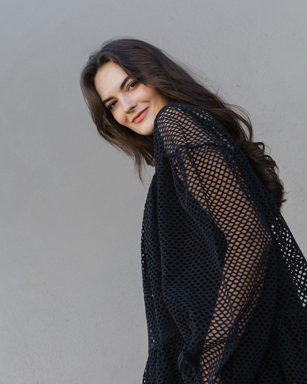 Woman wearing a black fishnet top against a plain background